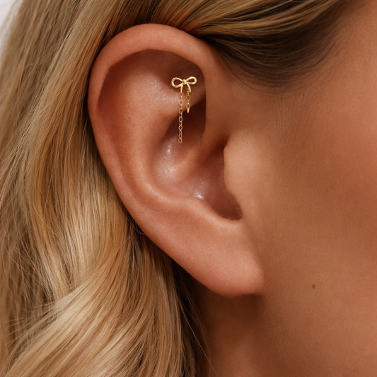 Gold bow cartilage earring with chain detail worn on helix piercing, dainty hypoallergenic ear jewelry