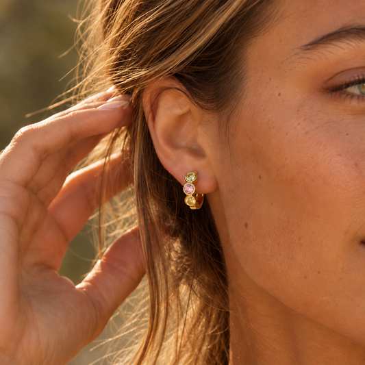 Chunky gold huggie earring with three colorful zirconia stones worn on ear