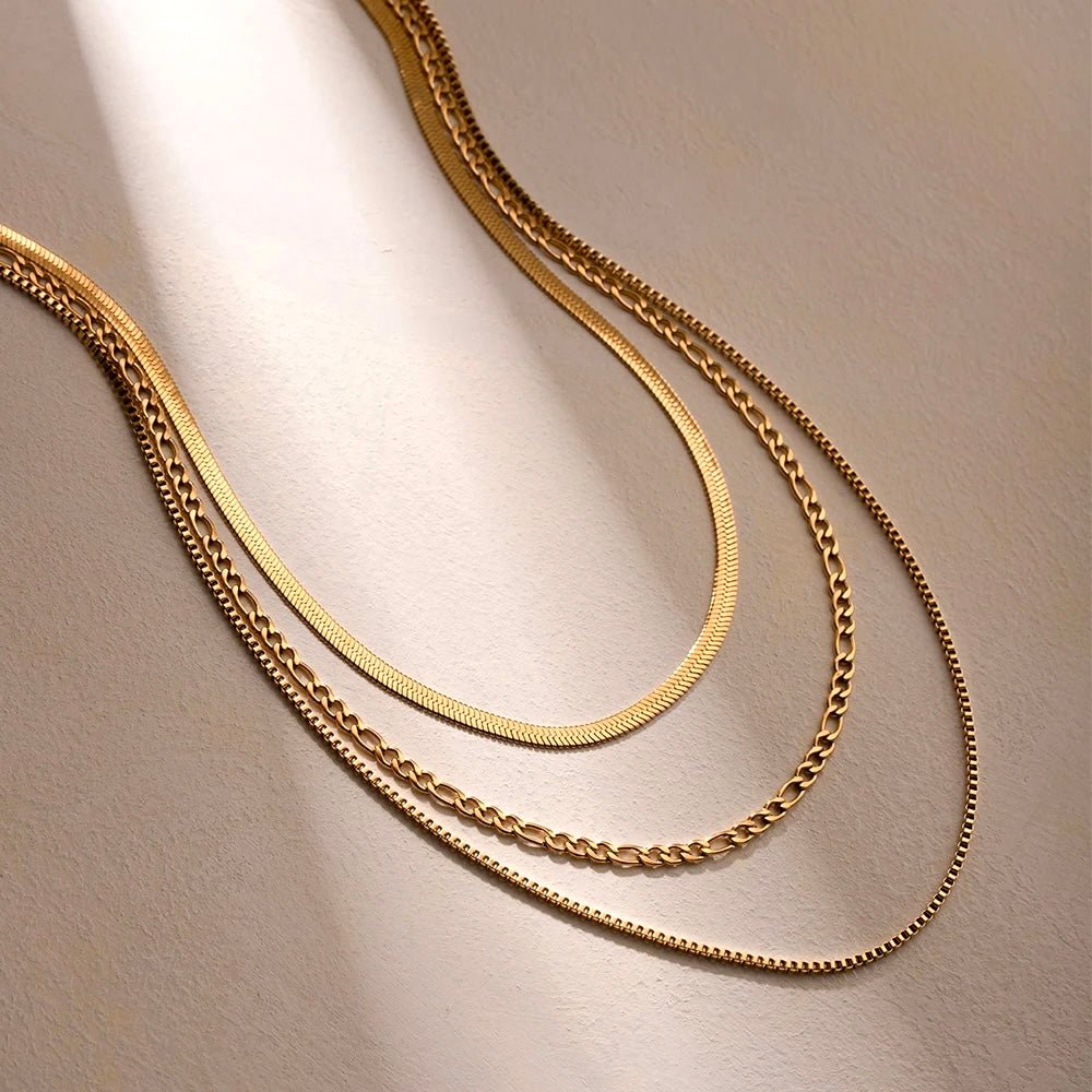 Flatlay showing layered gold chains – herringbone, figaro & cable