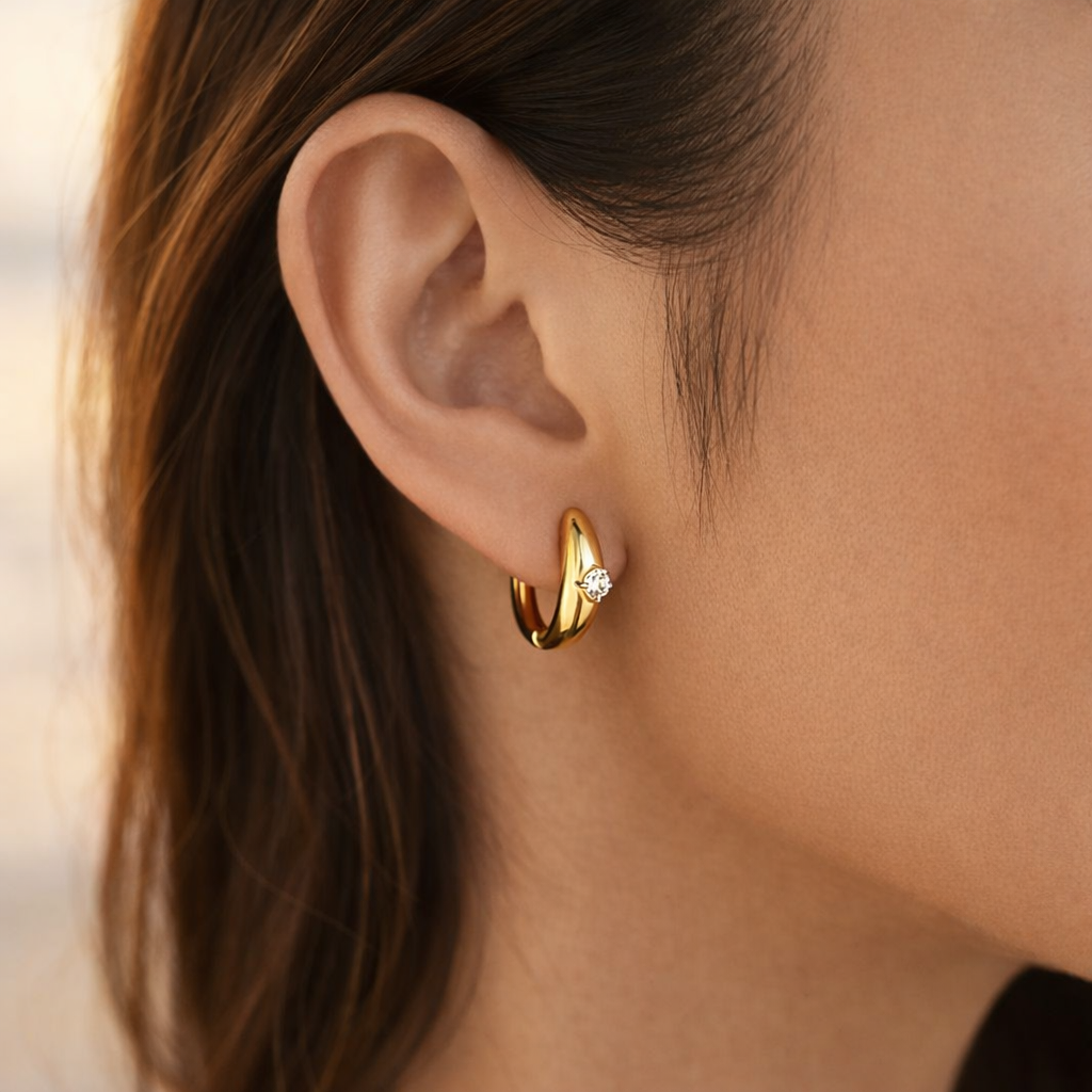 Gold huggie hoop earrings with white crystal worn on ear, minimalist waterproof stainless steel jewelry