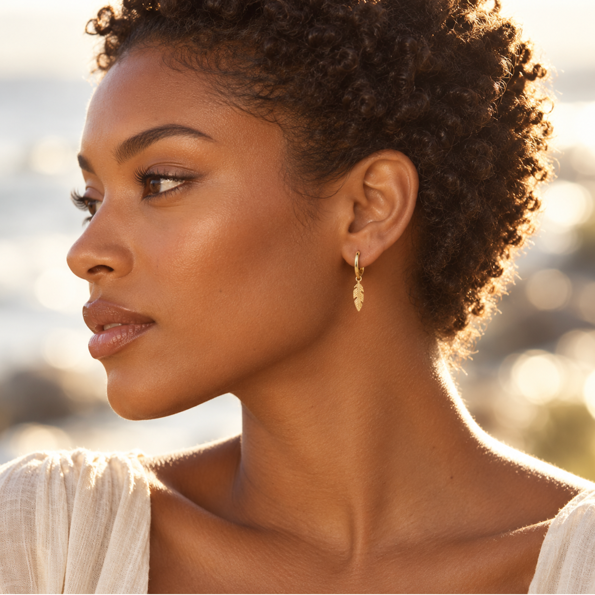 Side profile wearing boho gold feather earrings at golden hour