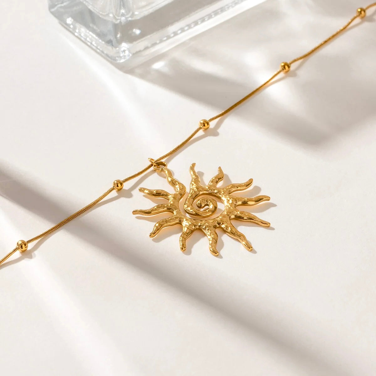 Boho-style gold sun charm necklace laid on a light surface