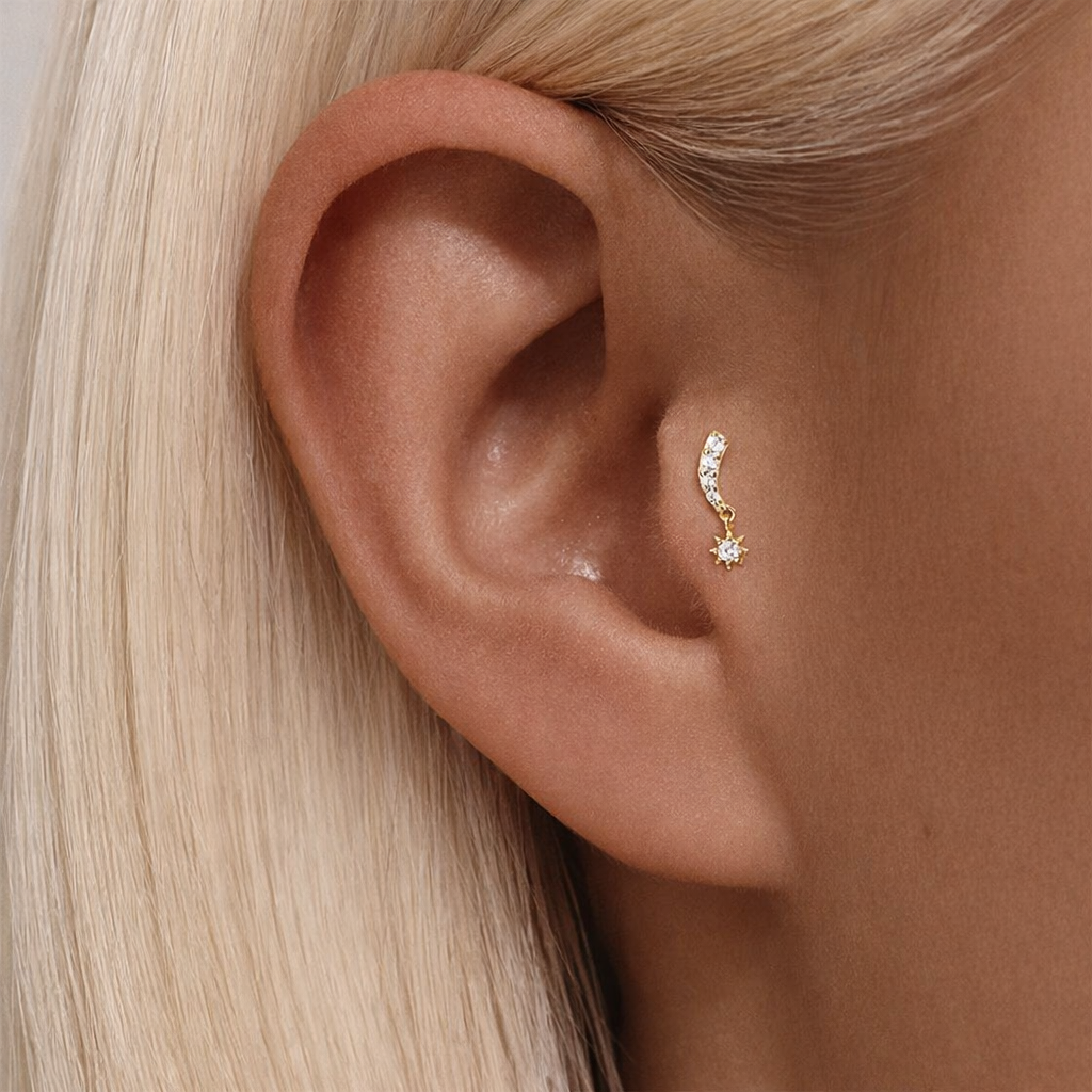 Celeste Curve gold cartilage stud worn on tragus piercing with curved zirconia design and star drop