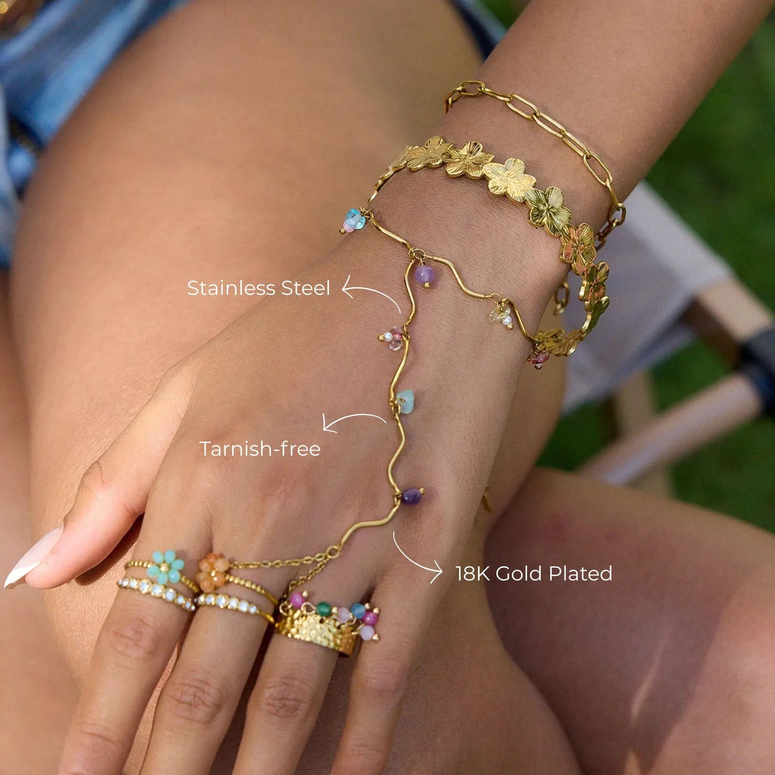 Model wearing gold hand chain bracelet with colorful beads and layered gold jewelry
