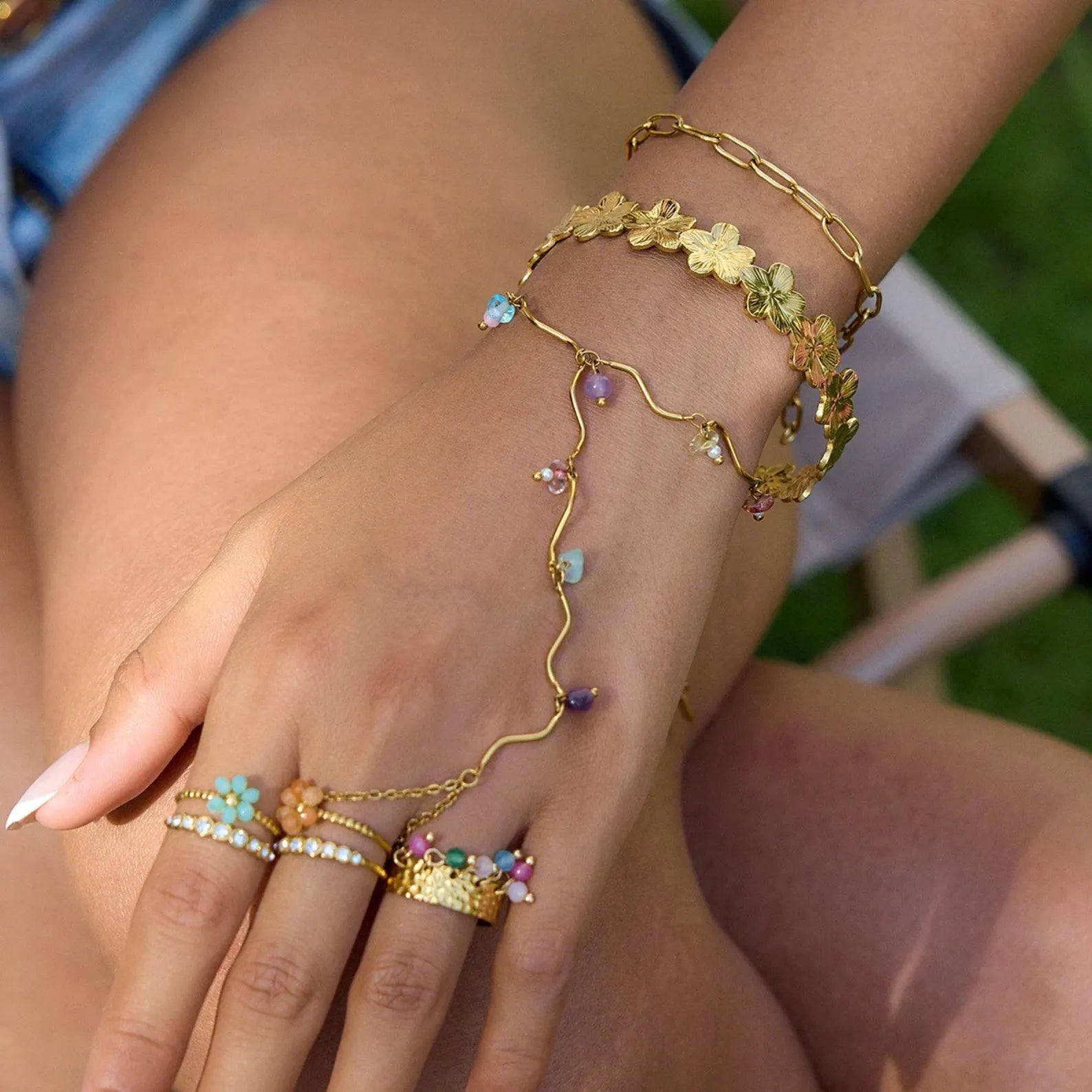 Model wearing gold hand chain bracelet with colorful beads and layered gold jewelry