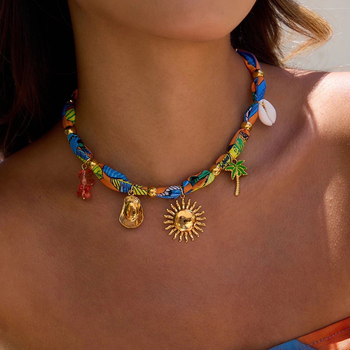 Woman wearing a fabric choker with gold-plated tropical charms, styled for a sunny vacation look.