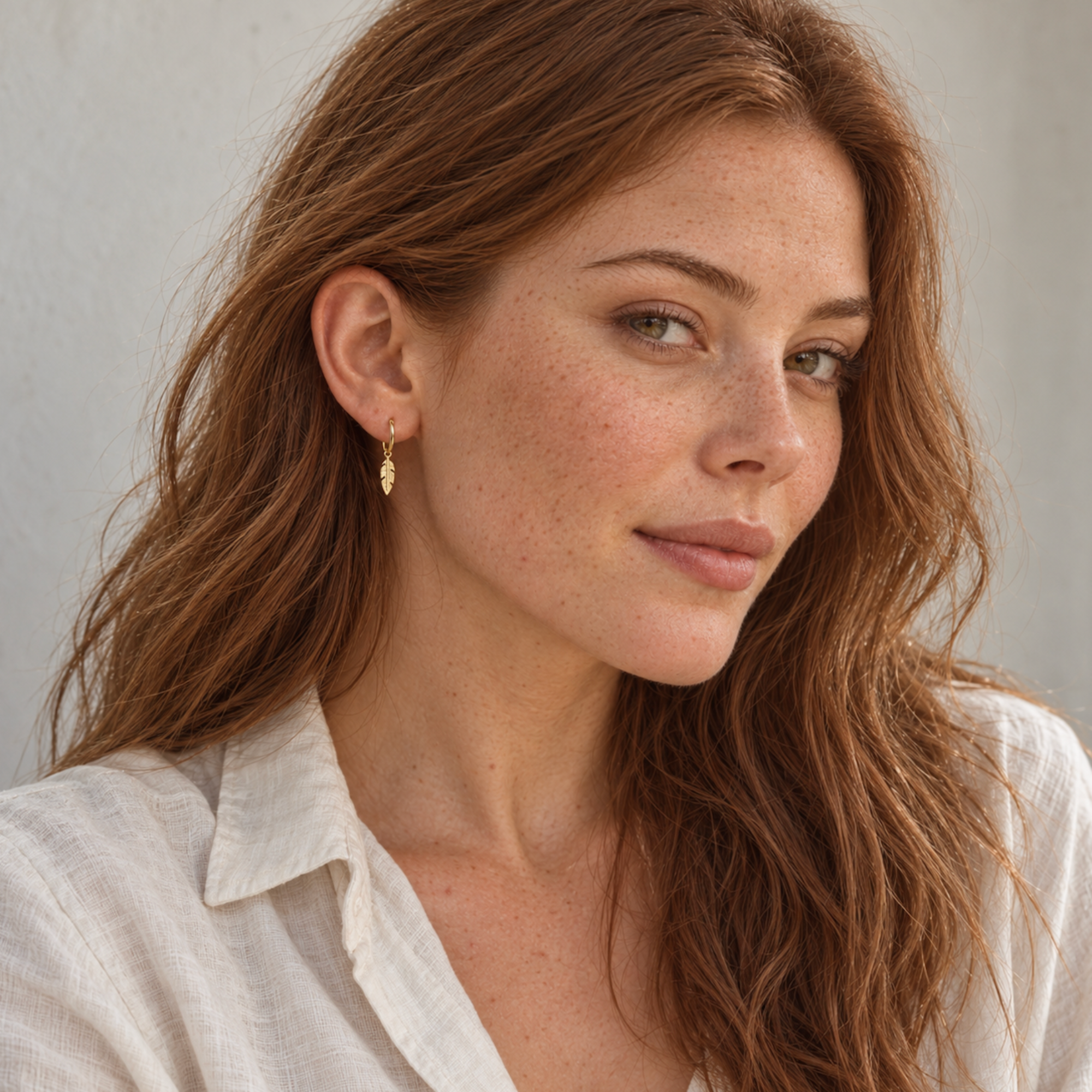 Small gold feather hoop earrings styled with a white linen shirt