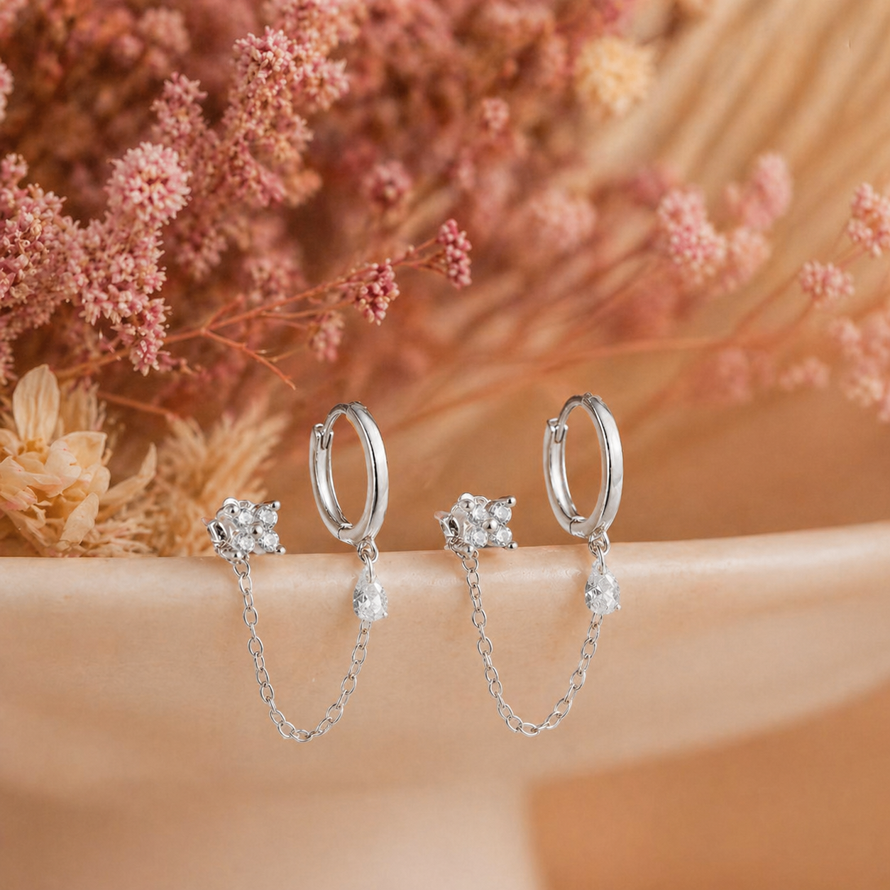 Pair of silver double piercing chain earrings with CZ stud and hoop on soft neutral background