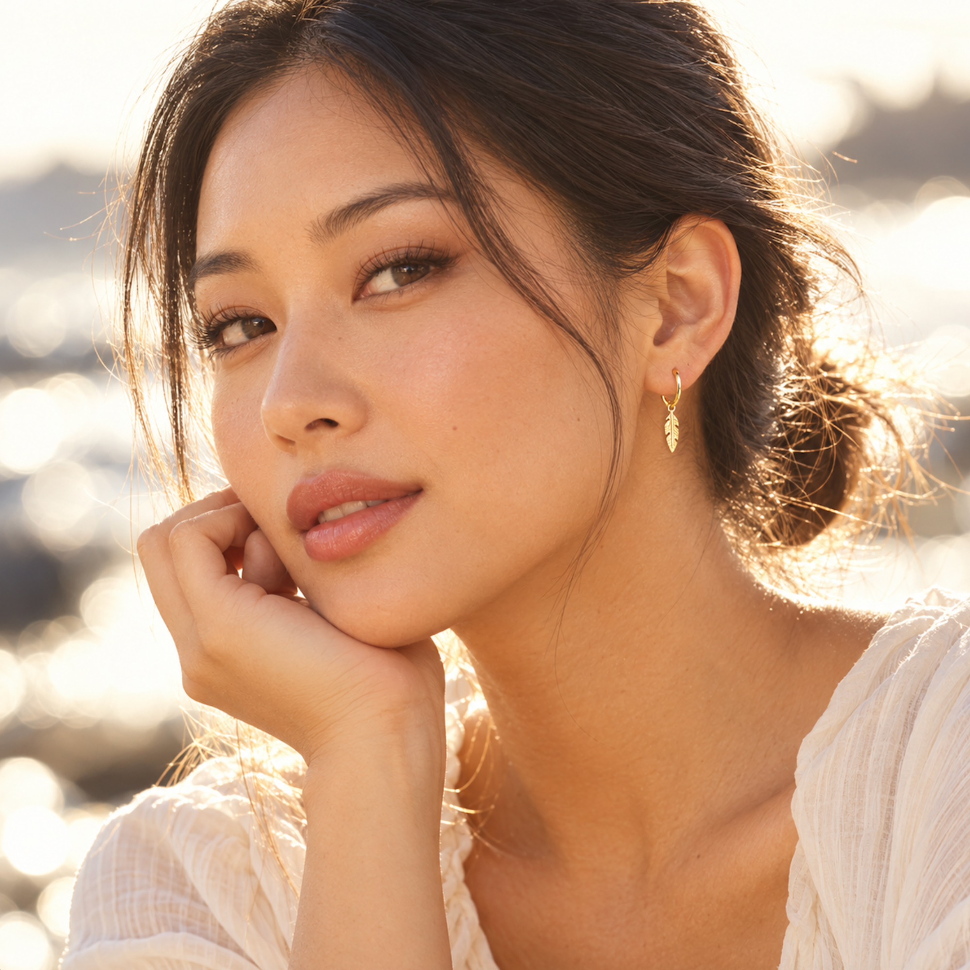 Woman wearing gold feather charm hoop earrings on a sunlit beach