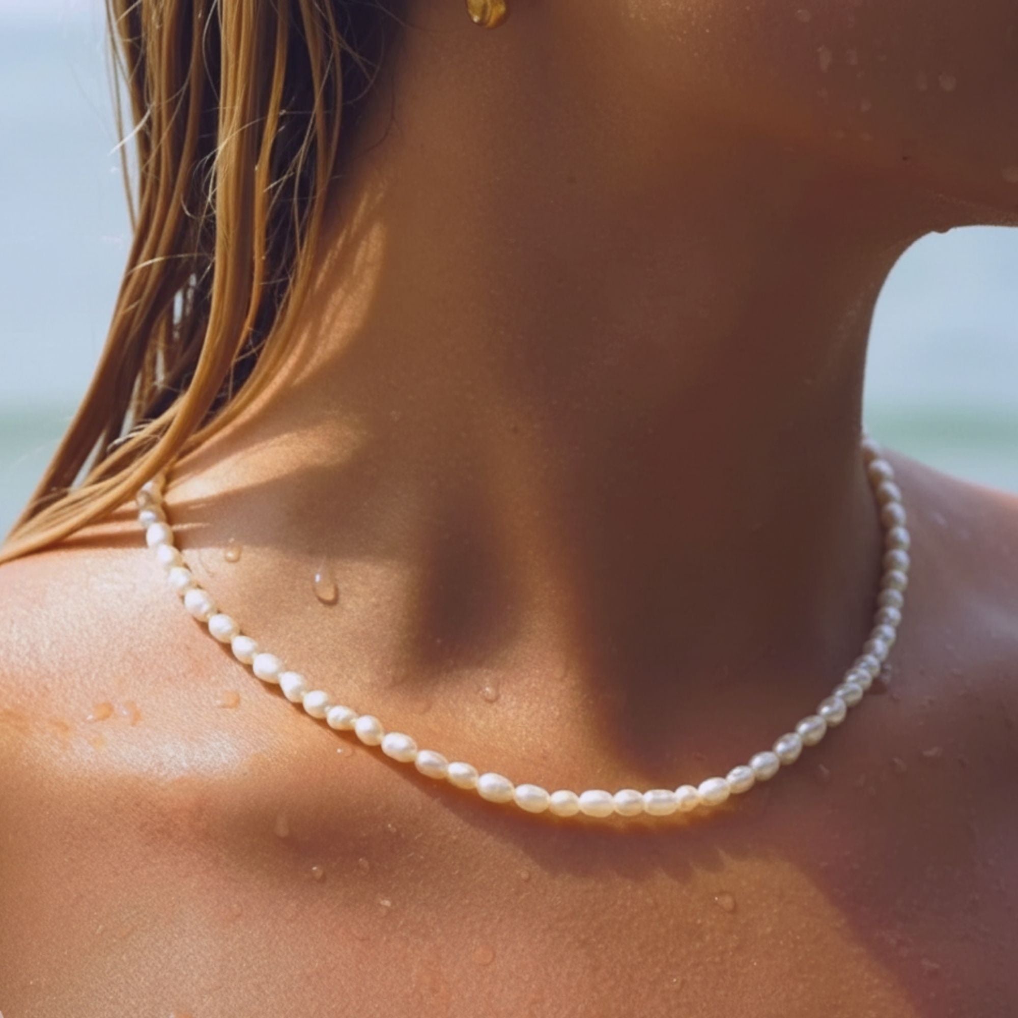  A wet caucasian model wearing the freshwater pearl necklace from Beach Bloom Jewelry at the beach.
