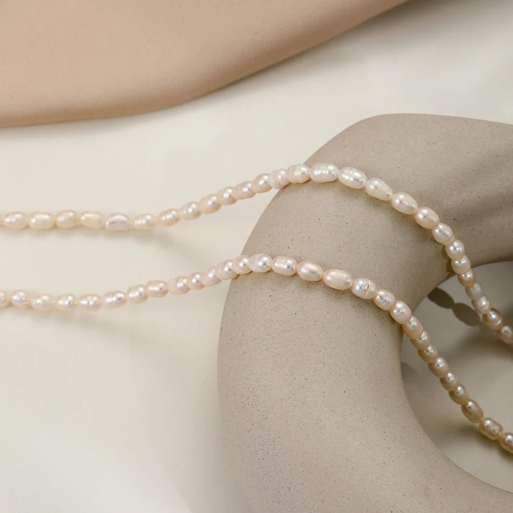 Draped flatlay of the Freshwater Pearl Choker with delicate chain on light fabric.