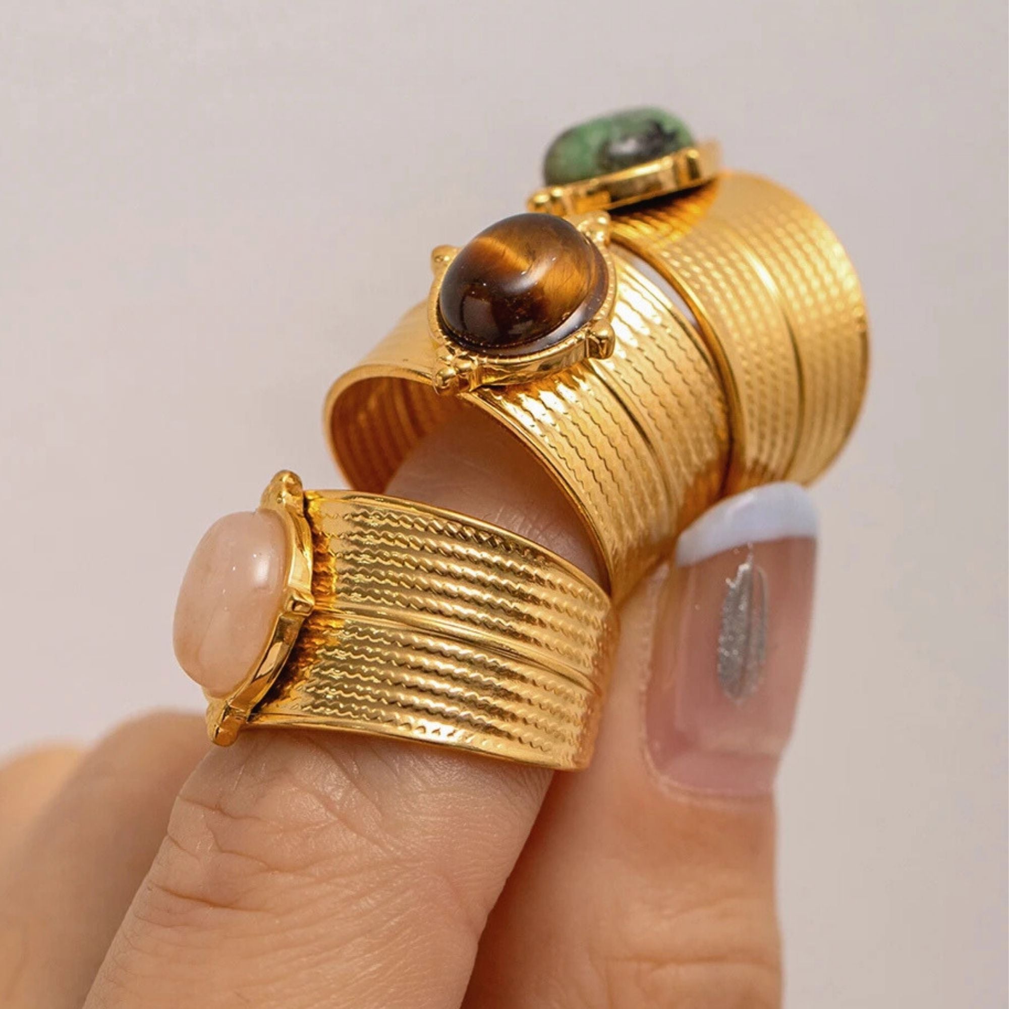 Gold adjustable cuff rings with Rose Quartz, Tiger’s Eye, and Green Jasper stacked on finger