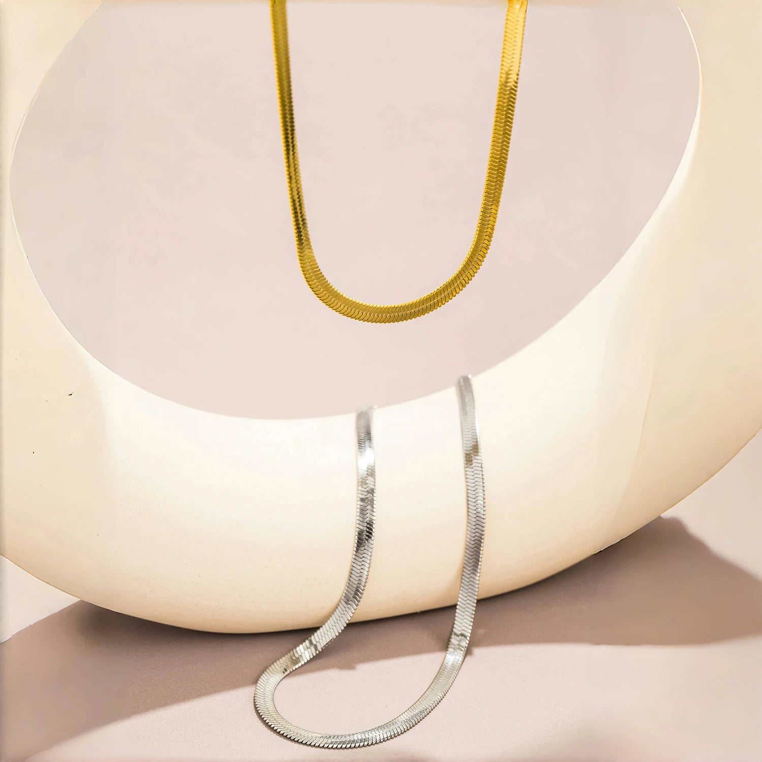 Gold and silver snake chain necklaces displayed on a minimalist ceramic stand