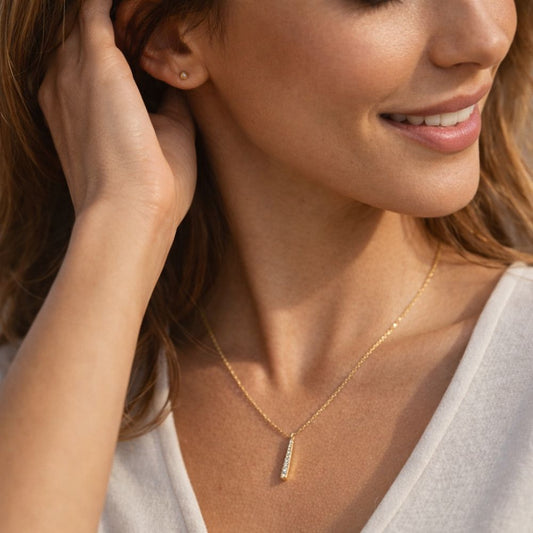 Close-up lifestyle shot of dainty gold bar pendant necklace worn by woman