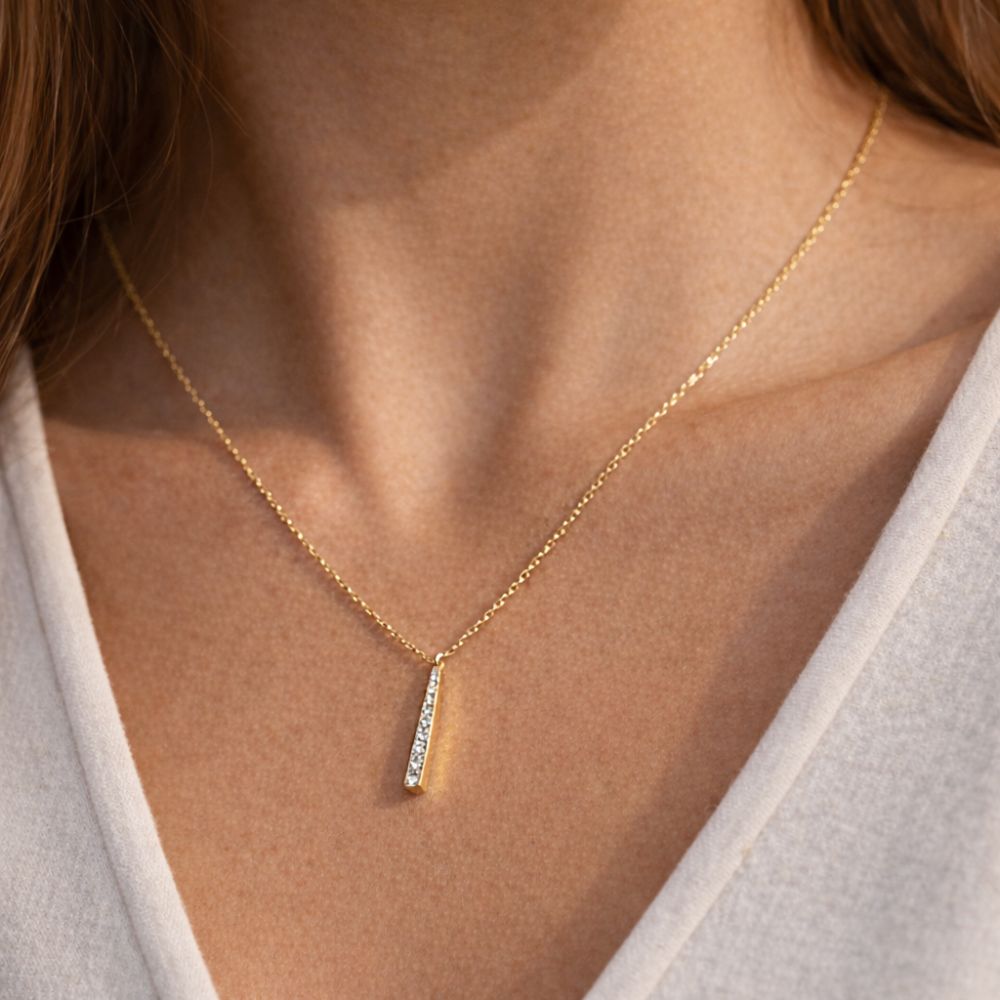 Detail view of minimalist gold bar necklace on woman neckline stainless steel jewelry
