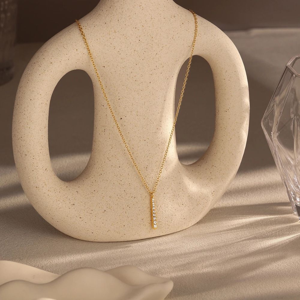Gold bar pendant necklace displayed on ceramic stand minimalist jewelry styling