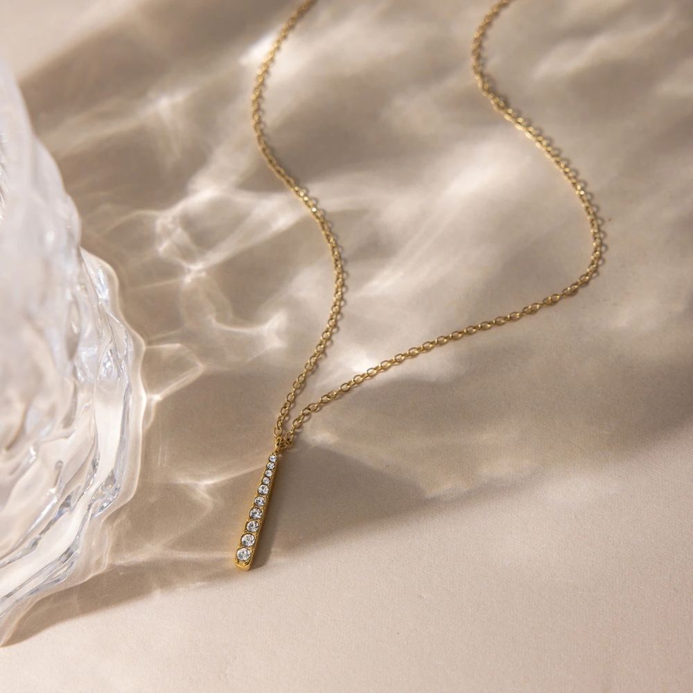 Minimalist gold bar pendant necklace with reflective water light aesthetic background