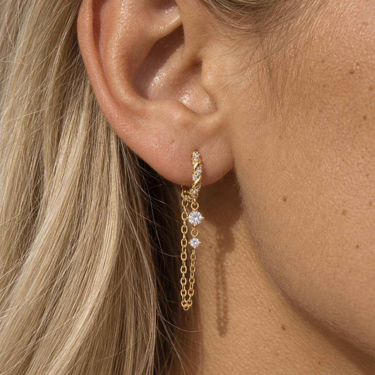 Gold twisted chain drop earring with zircon stones worn on a woman’s ear
