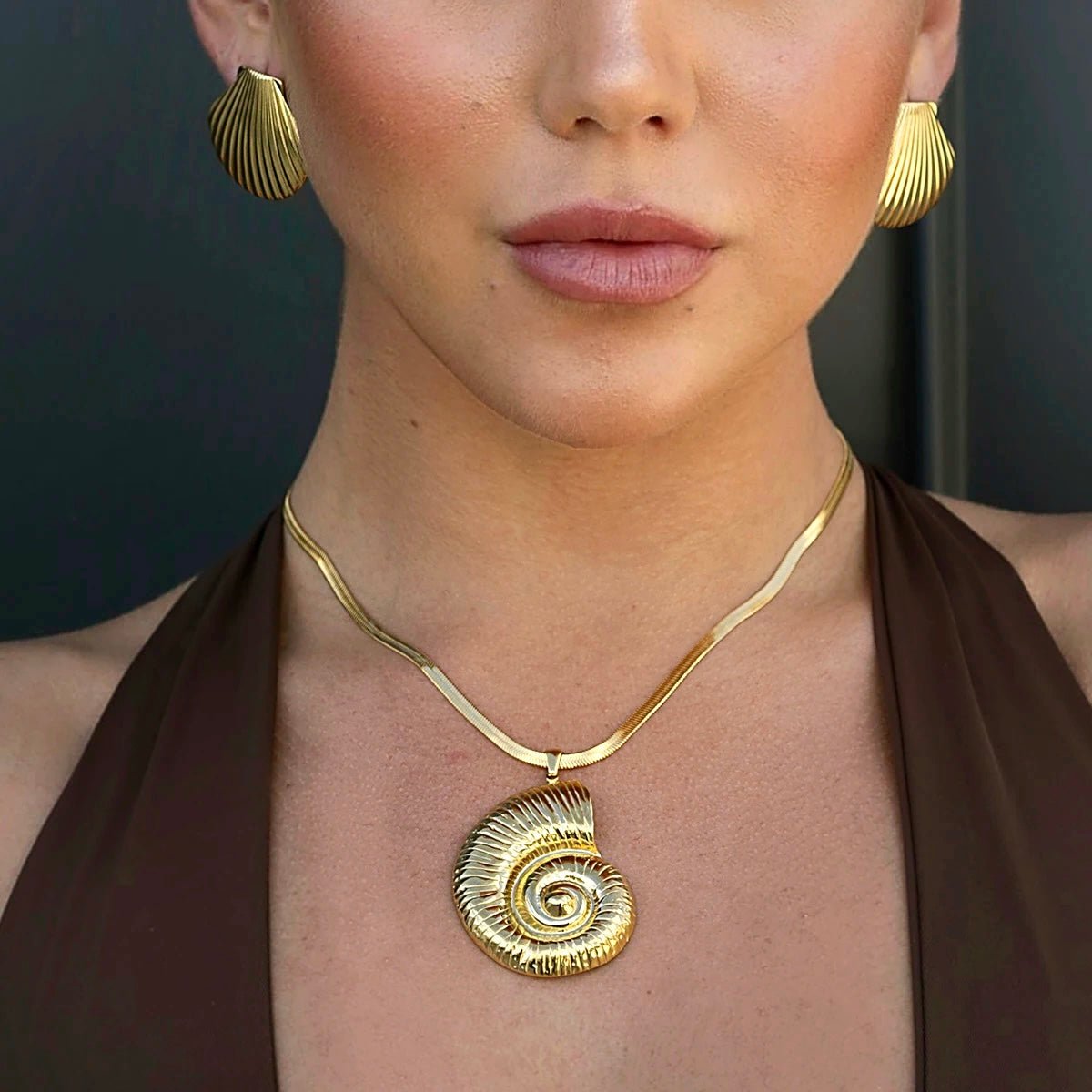 Woman wearing gold conch pendant necklace and seashell earrings for a beachy look
