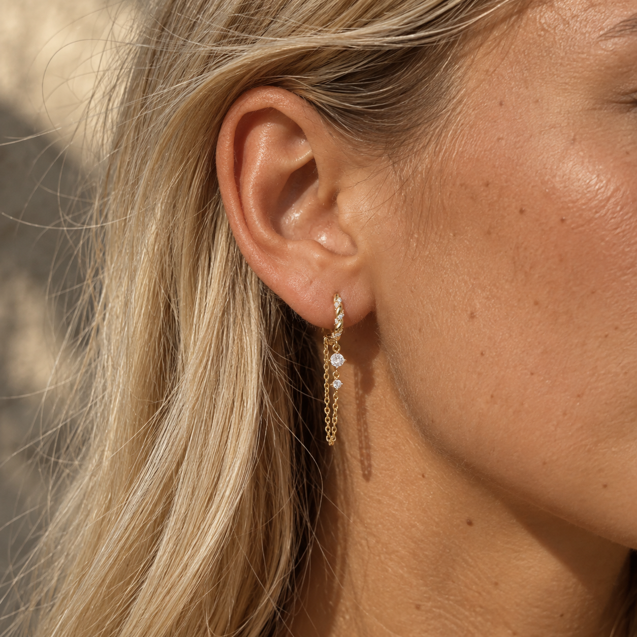 Gold crystal chain drop earrings worn on a woman’s ear