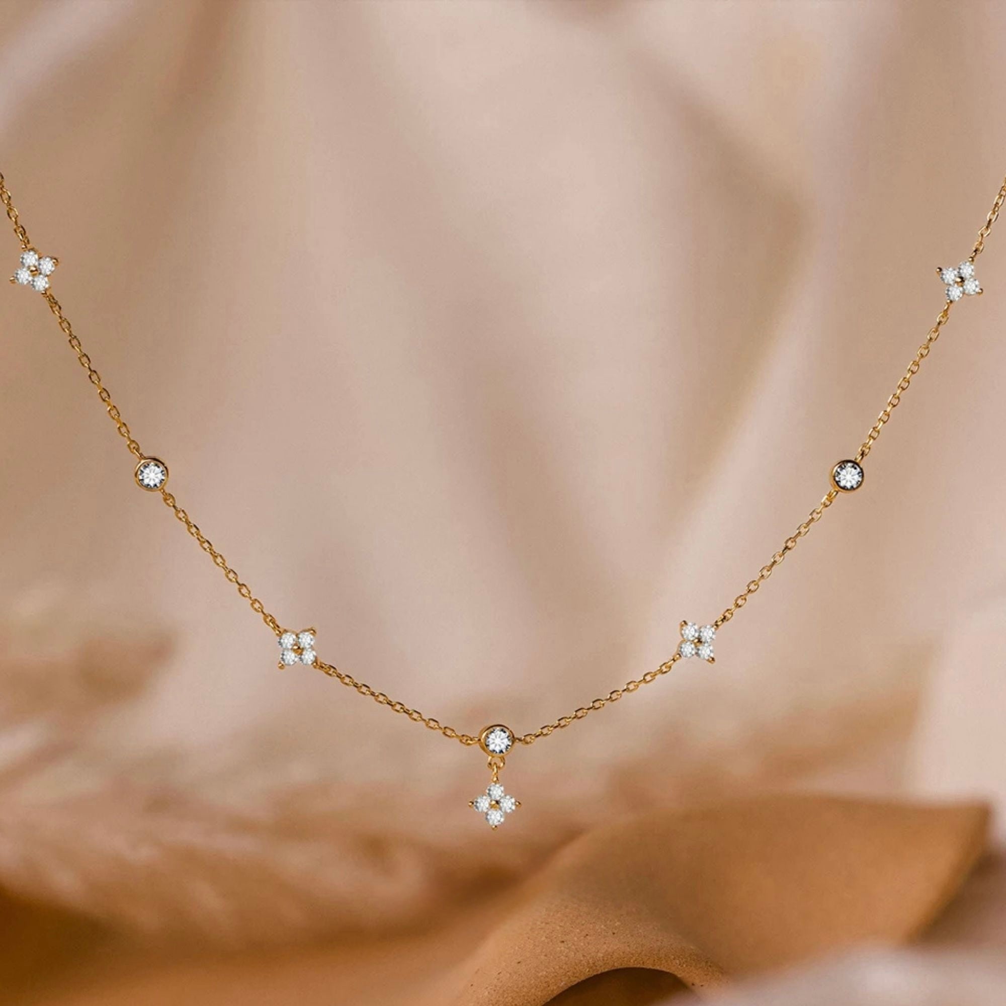 Woman wearing gold daisy diamond station necklace with zircon charms on a beige off-shoulder top