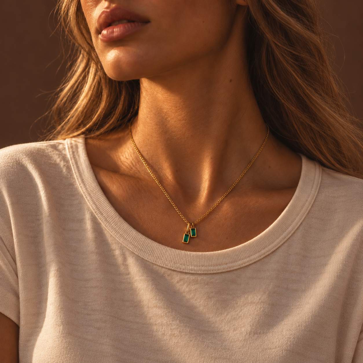 Close-up of a gold double emerald green pendant necklace in warm evening light with soft shadows.