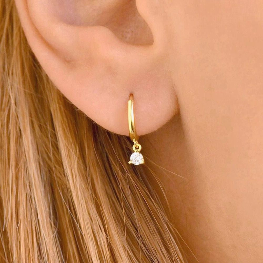 Close-up of a gold huggie earring featuring a delicate dangling zirconia stone.