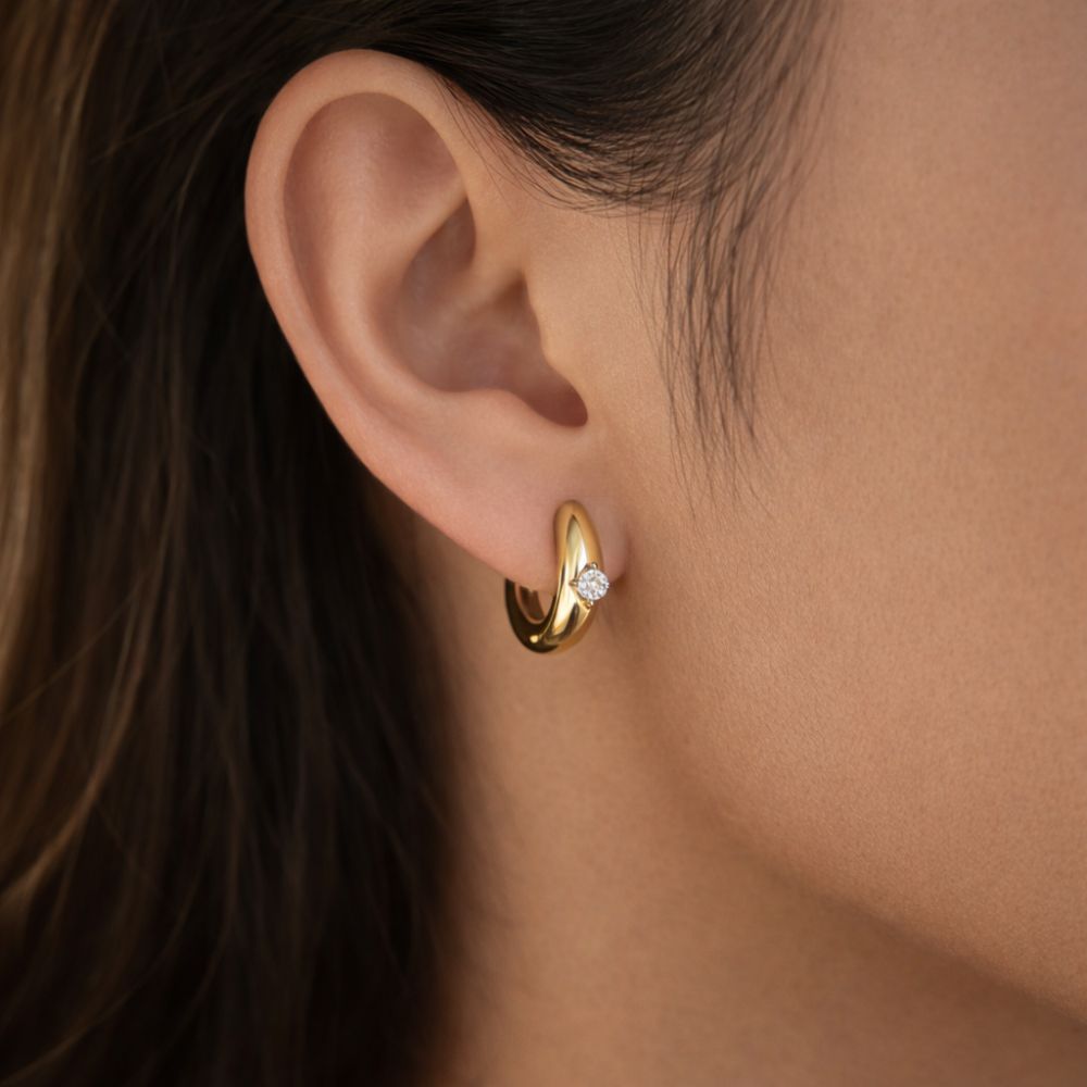 Close up of gold huggie hoop earrings with white zircon worn on ear