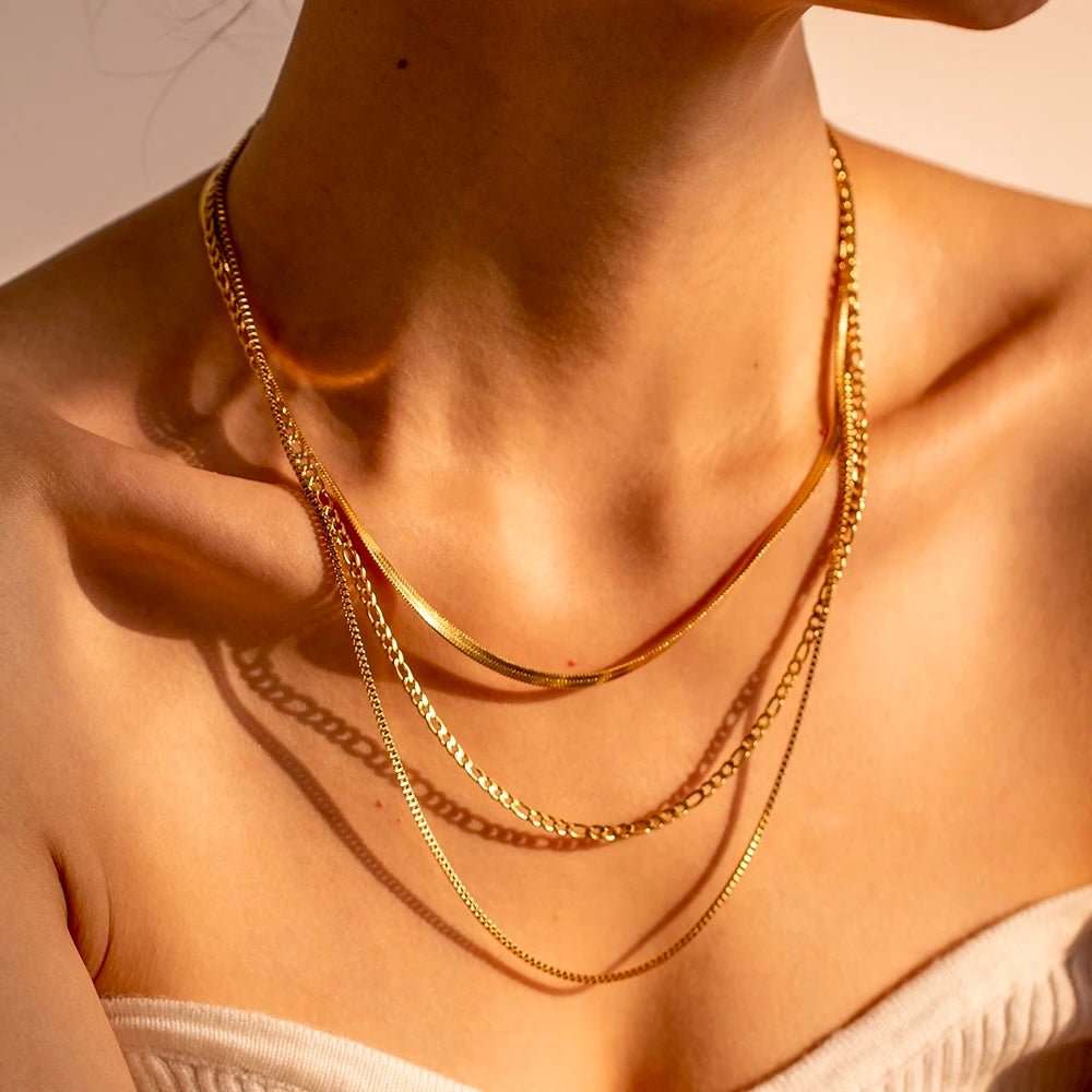 Woman wearing gold layered necklace with herringbone, figaro & cable chain