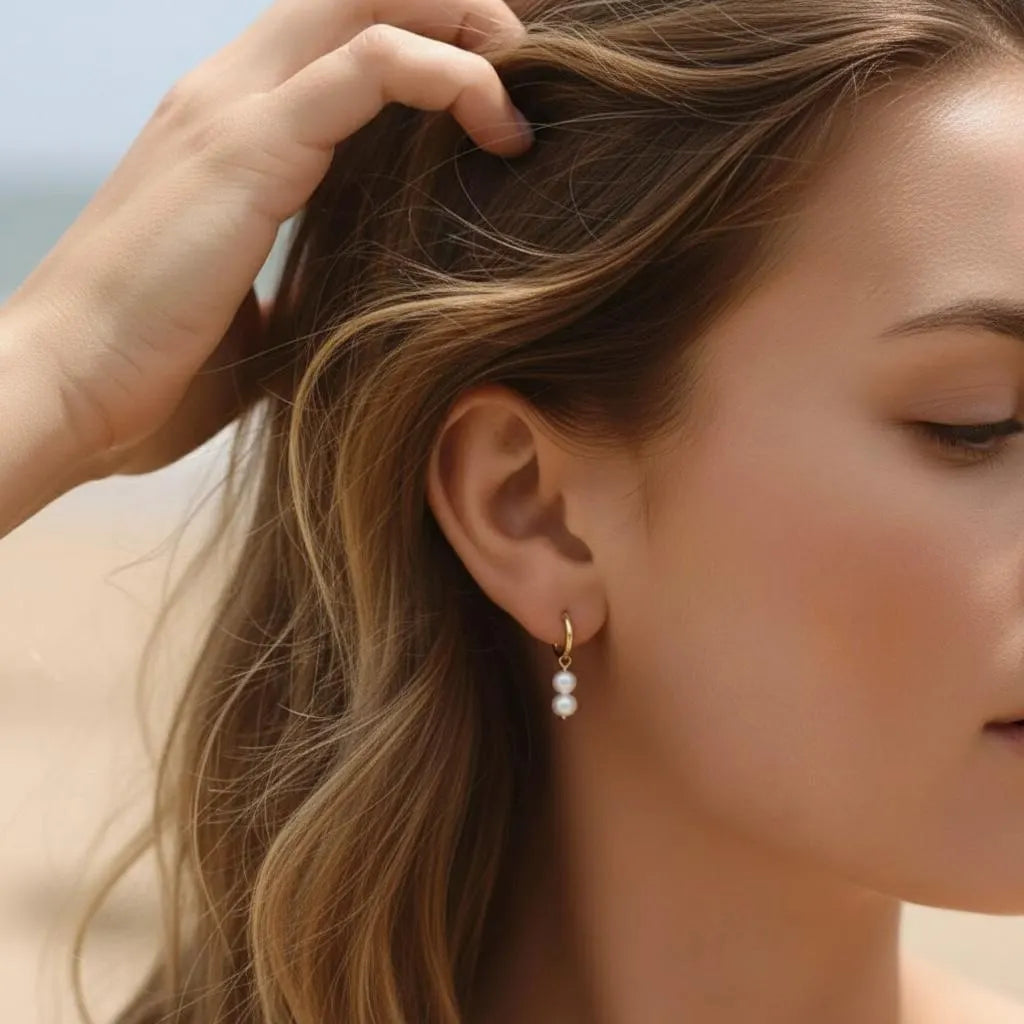 Gold double pearl drop hoop earrings worn at the beach, minimalist pearl jewelry