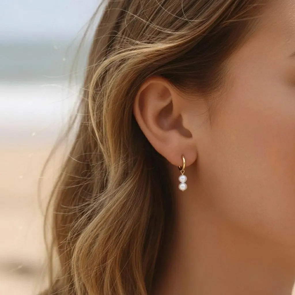 Minimalist pearl hoop earrings with double pearls worn by woman at the beach