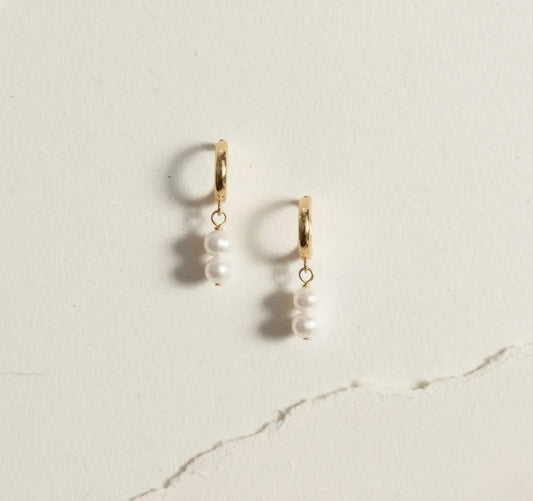 Gold hoop earrings with double pearl drops displayed on cream textured background