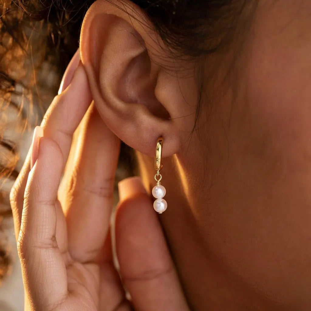 Gold hoop earrings with two pearls worn in warm sunset light, elegant feminine jewelry