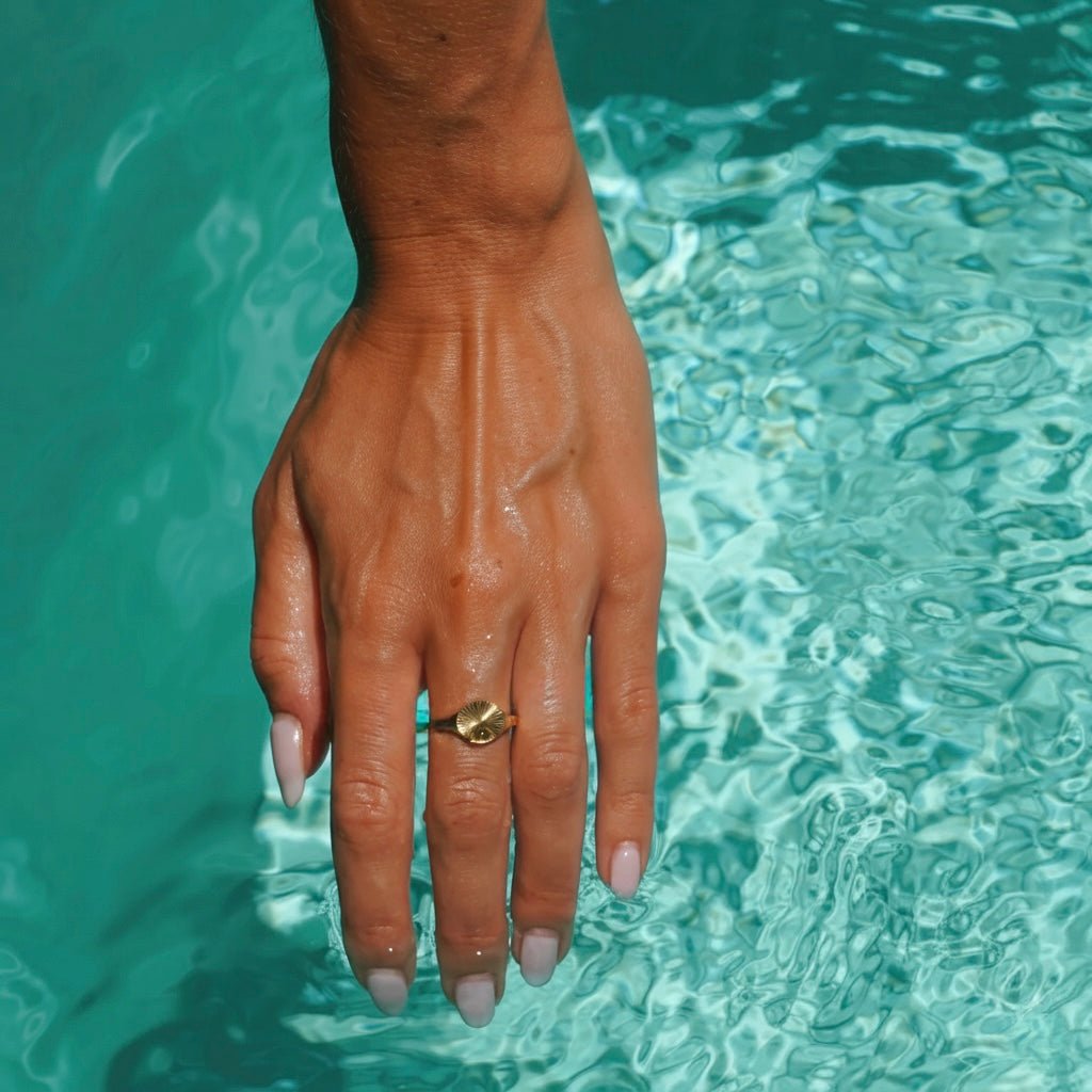 Hand over turquoise water wearing the Sunbeam Gold Signet Ring – waterproof 18K gold stainless steel jewelry by Beach Bloom Jewelry.