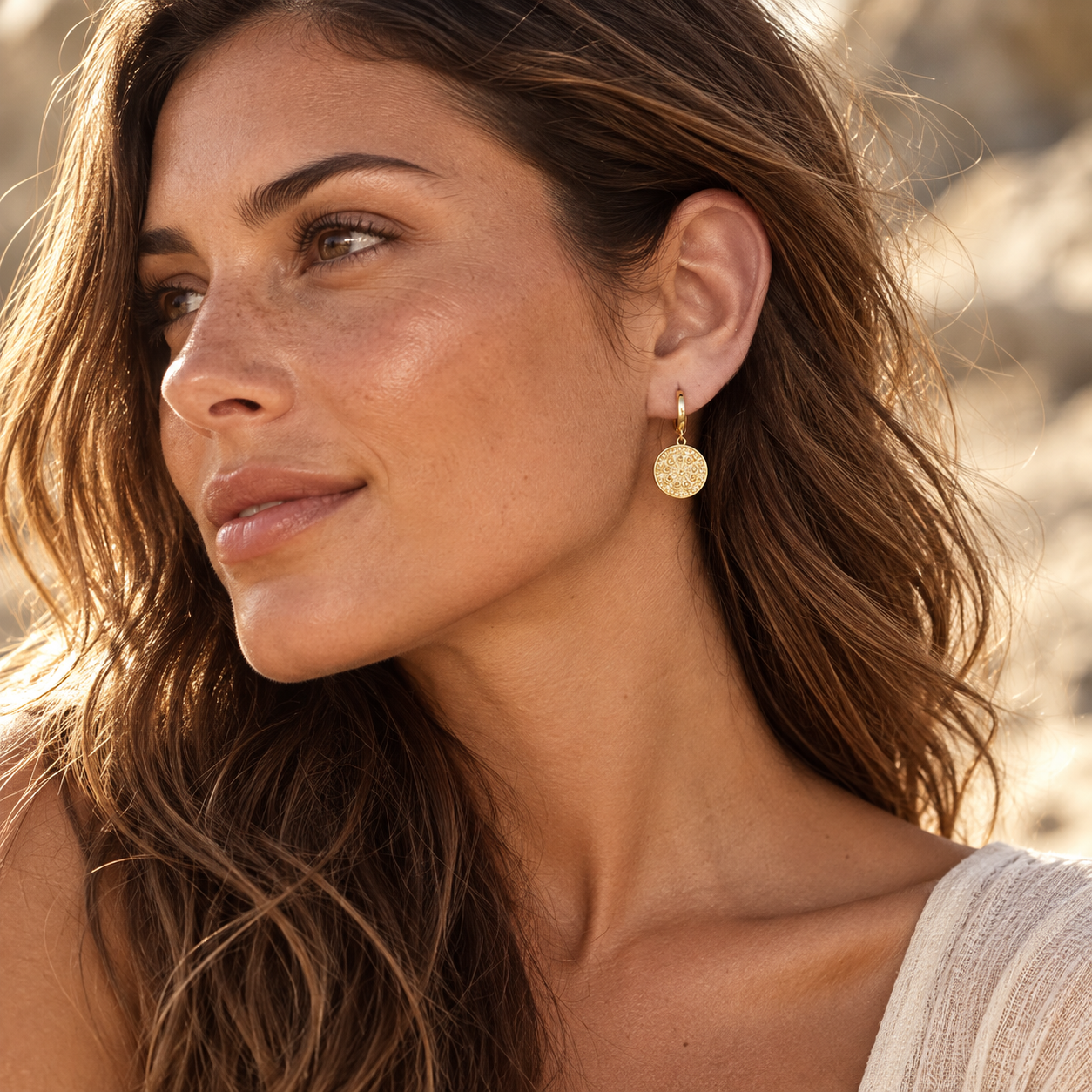 Brunette wearing gold plated medallion hoop earrings in natural sunlight