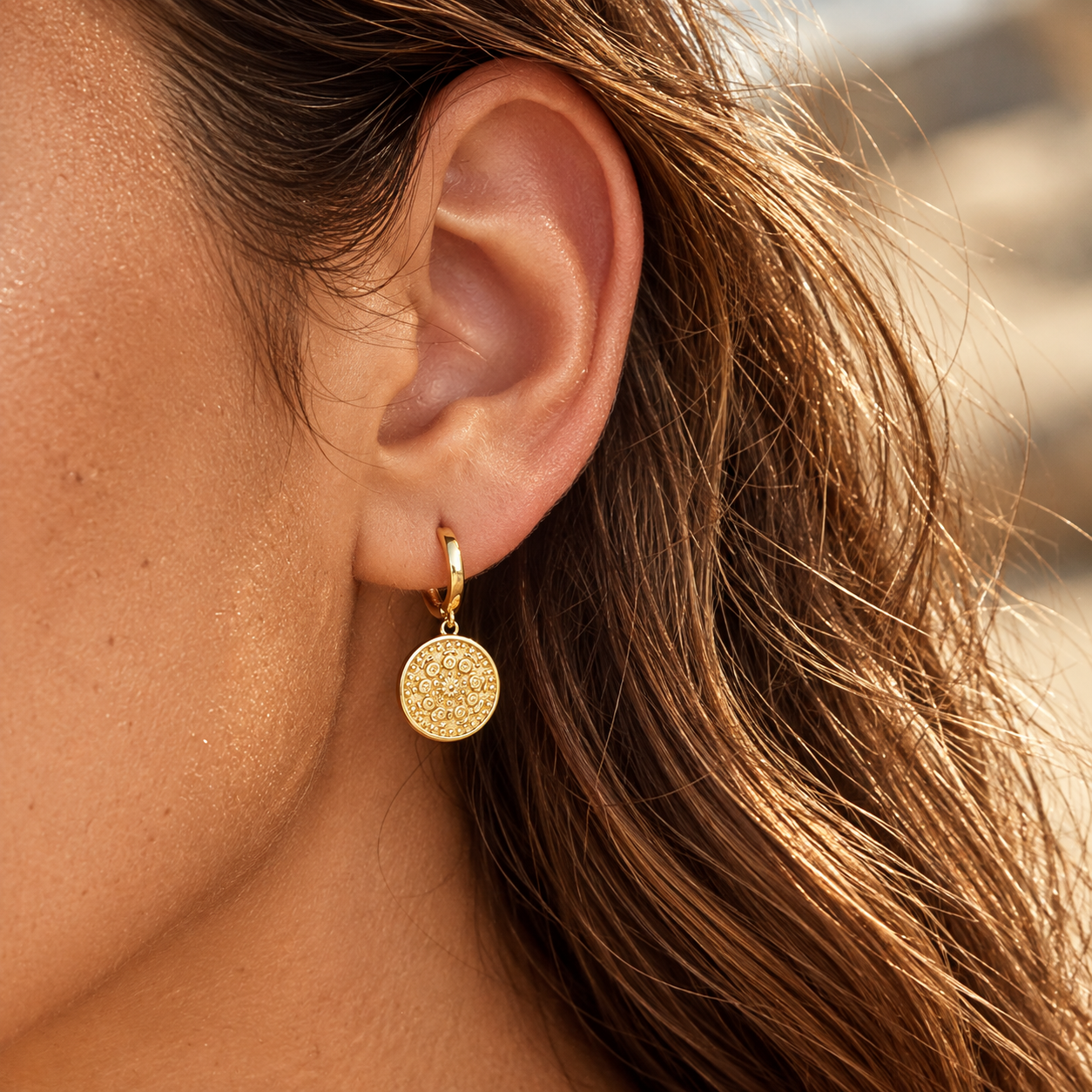 Close-up of a brunette wearing gold plated round charm hoop earrings with an ornate medallion pendant