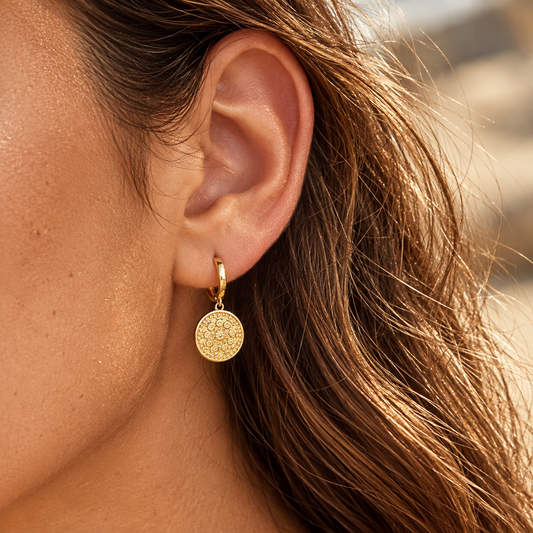Close-up of a brunette wearing gold plated round charm hoop earrings with an ornate medallion pendant