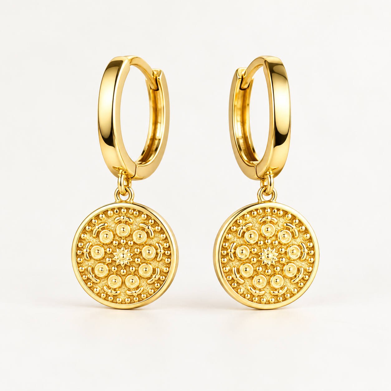 Pair of gold plated 925 sterling silver hoop earrings with textured round medallion charms on an ivory background