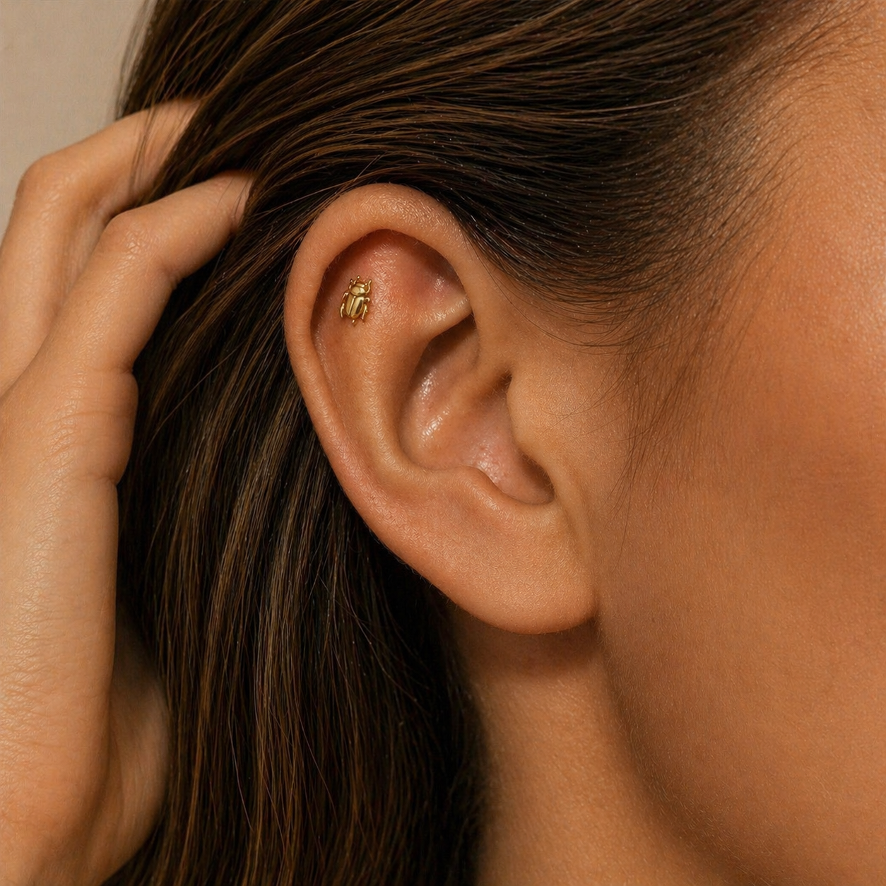 Gold scarab stud earring worn on helix piercing, elegant ear styling with hand in hair