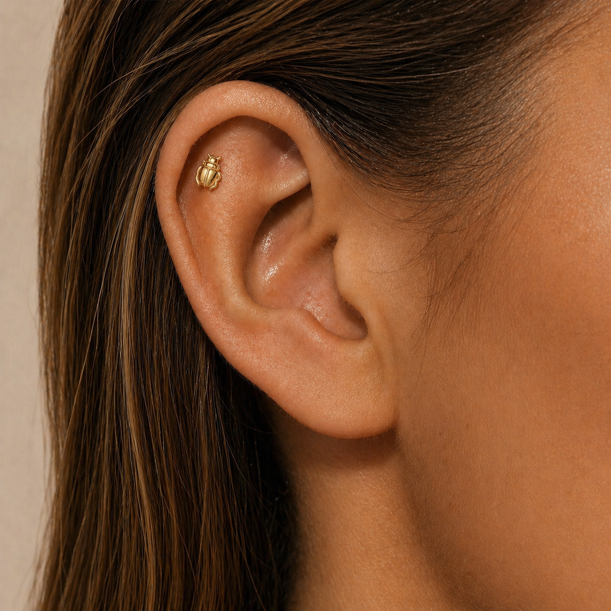 Gold scarab stud earring on ear, delicate cartilage jewelry for helix or flat piercing