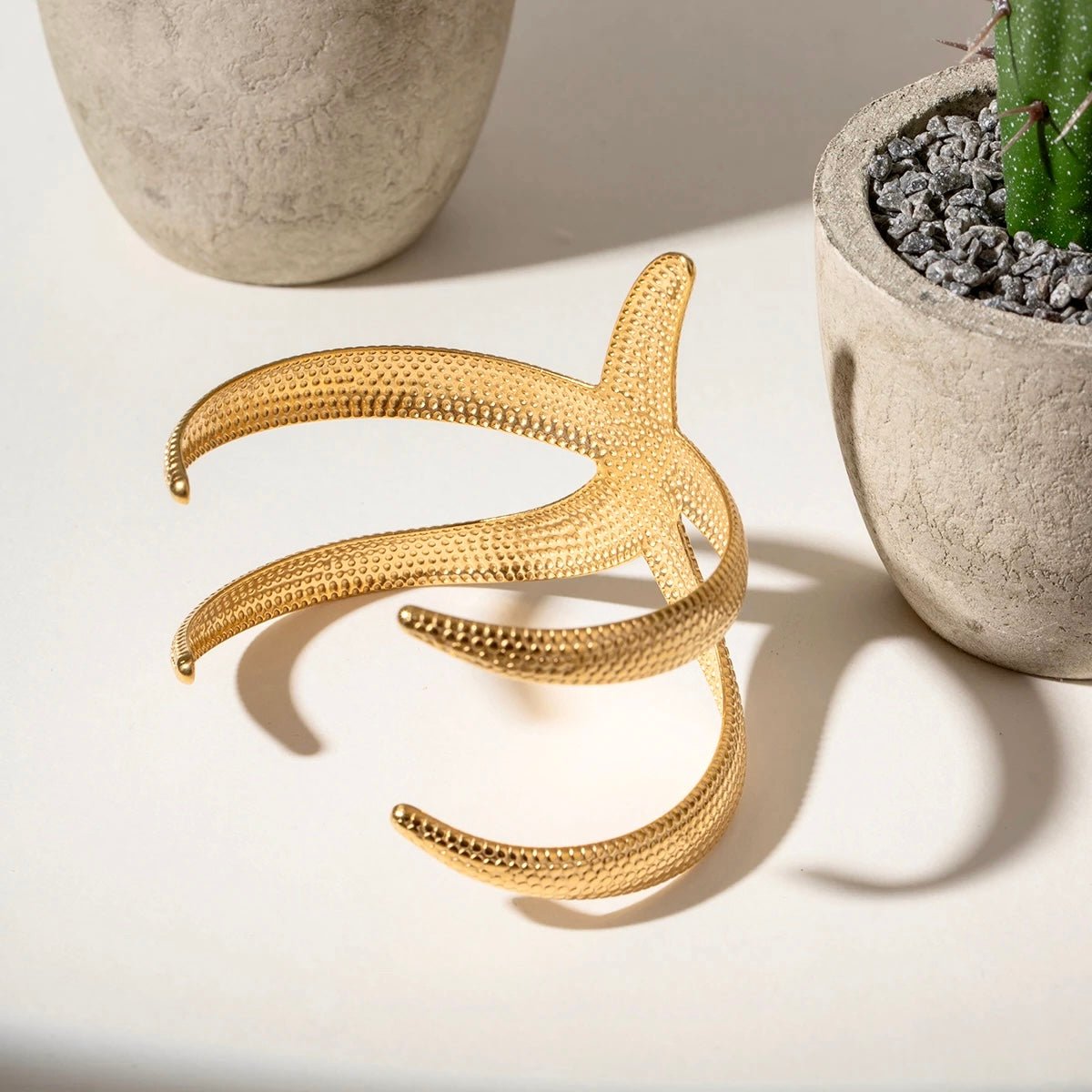 Textured gold starfish bracelet displayed next to cactus on white surface
