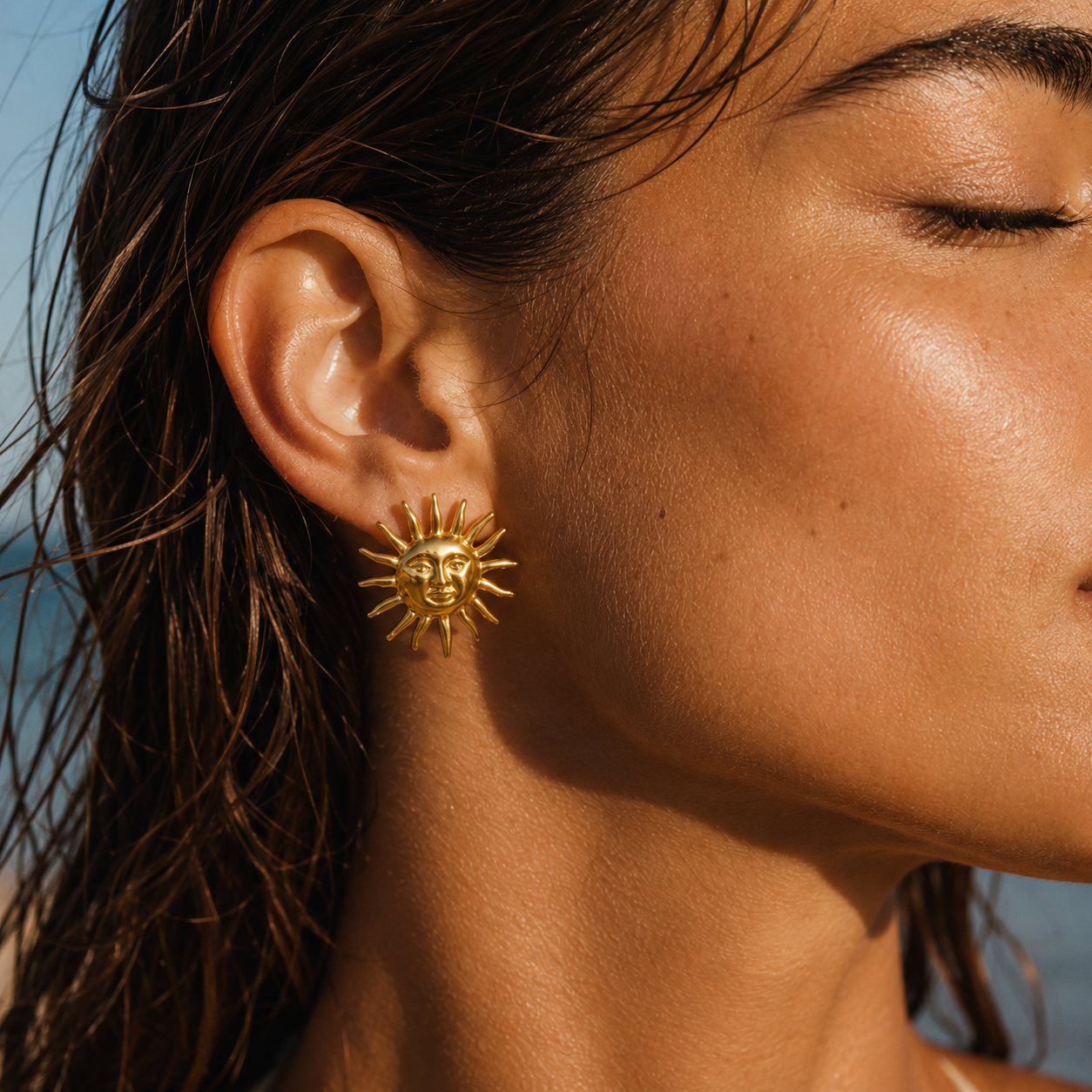 Close-up of gold sun statement earrings with celestial face design