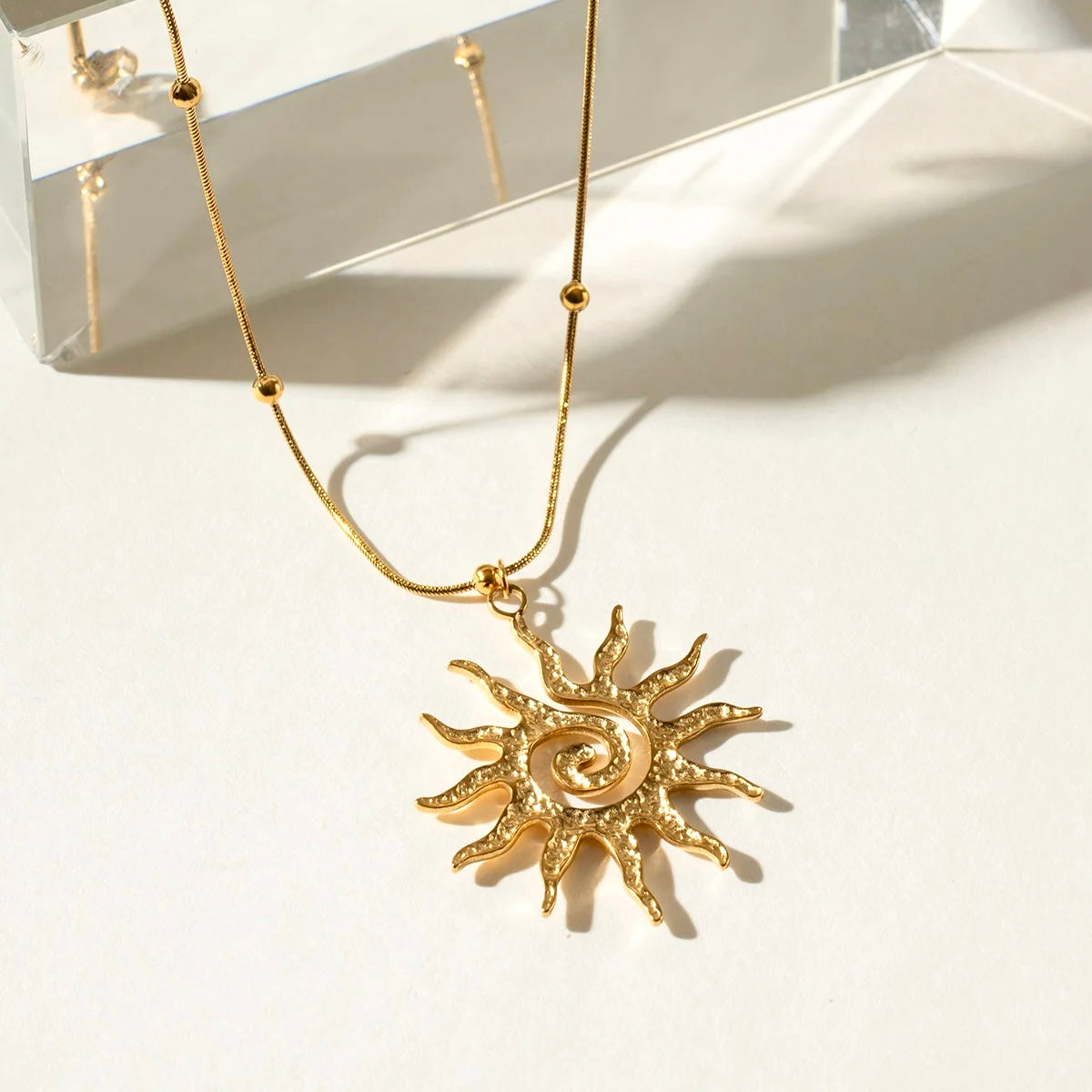 Flatlay of 18K gold sun pendant necklace with beaded chain