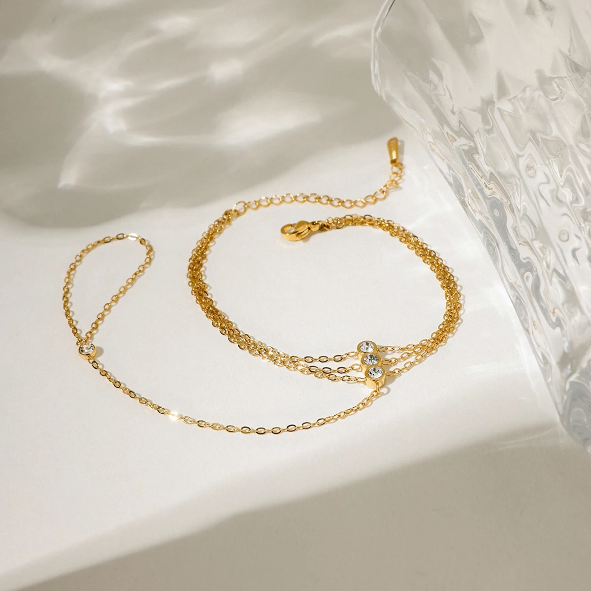 Gold Trio Hand Chain Bracelet displayed in a minimalist setting with glass reflections and delicate gold chains.