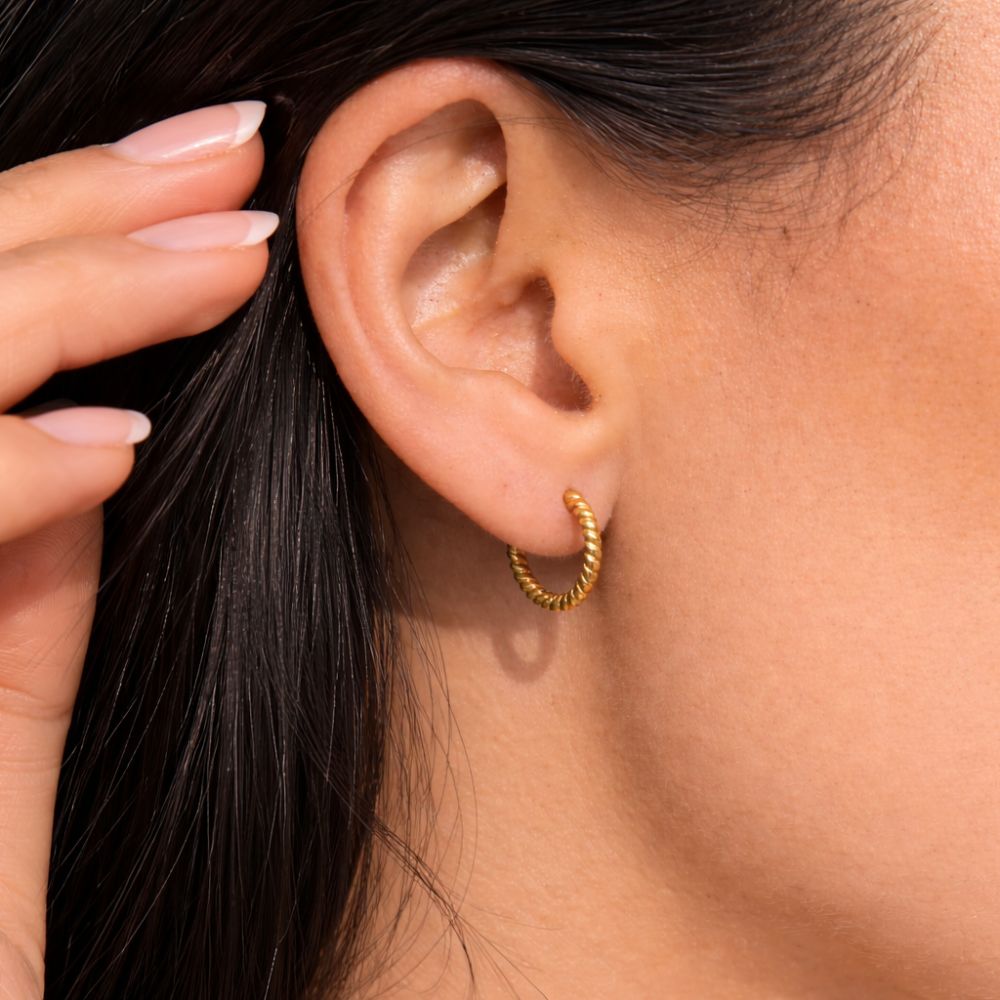 Woman wearing gold twisted hoop earrings, small rope texture hoop earrings on ear.