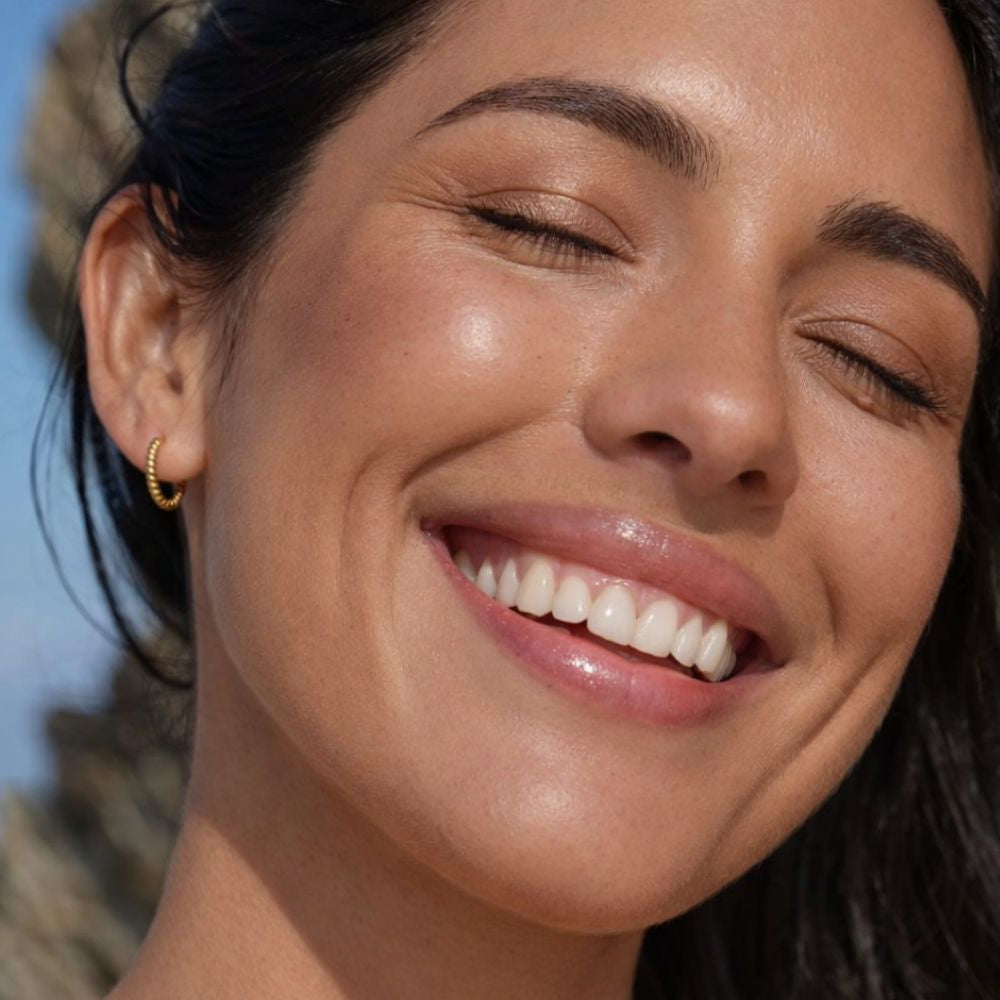 Woman smiling wearing gold twisted hoop earrings, elegant small gold huggie earrings.