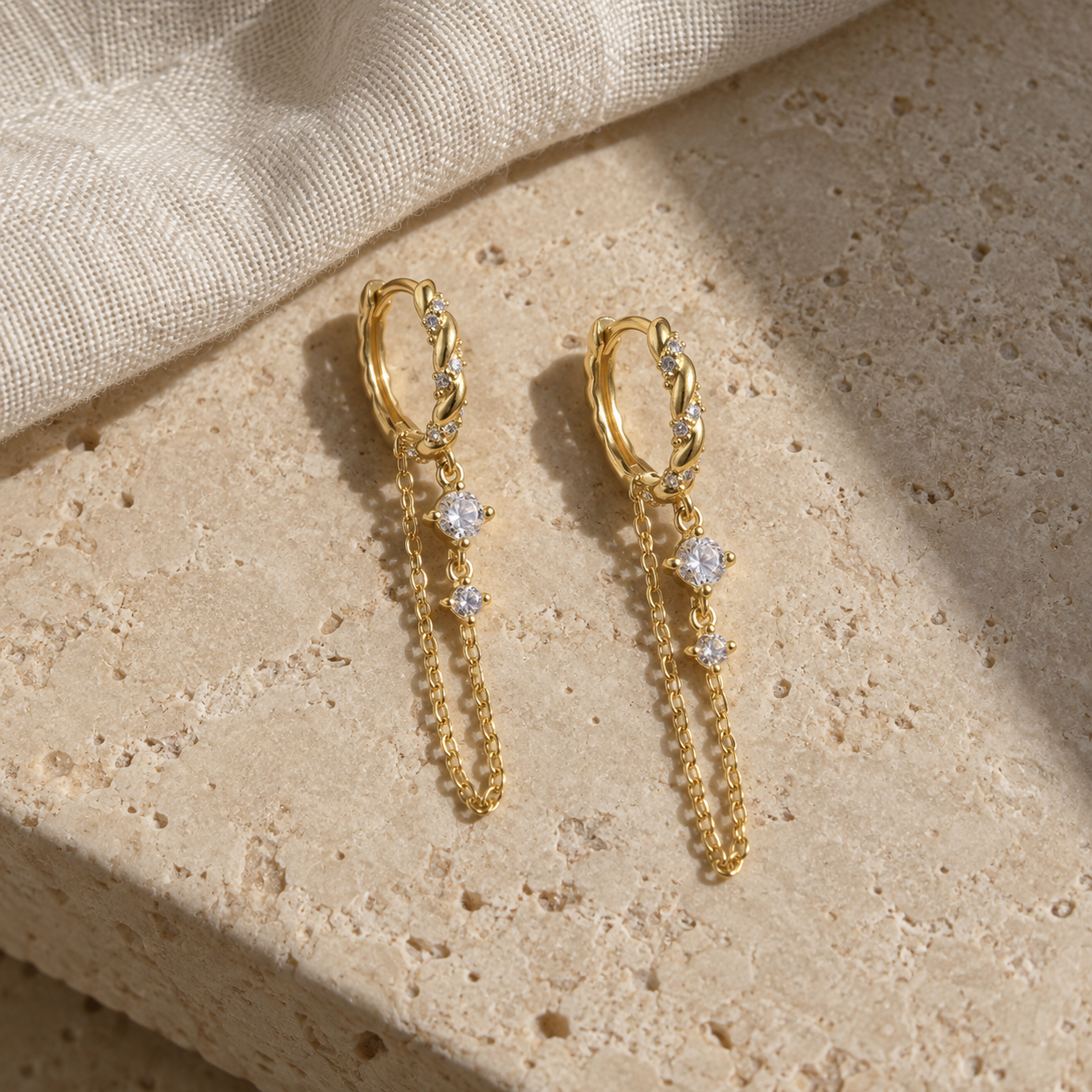 Gold zircon chain hoop earrings displayed on natural stone
