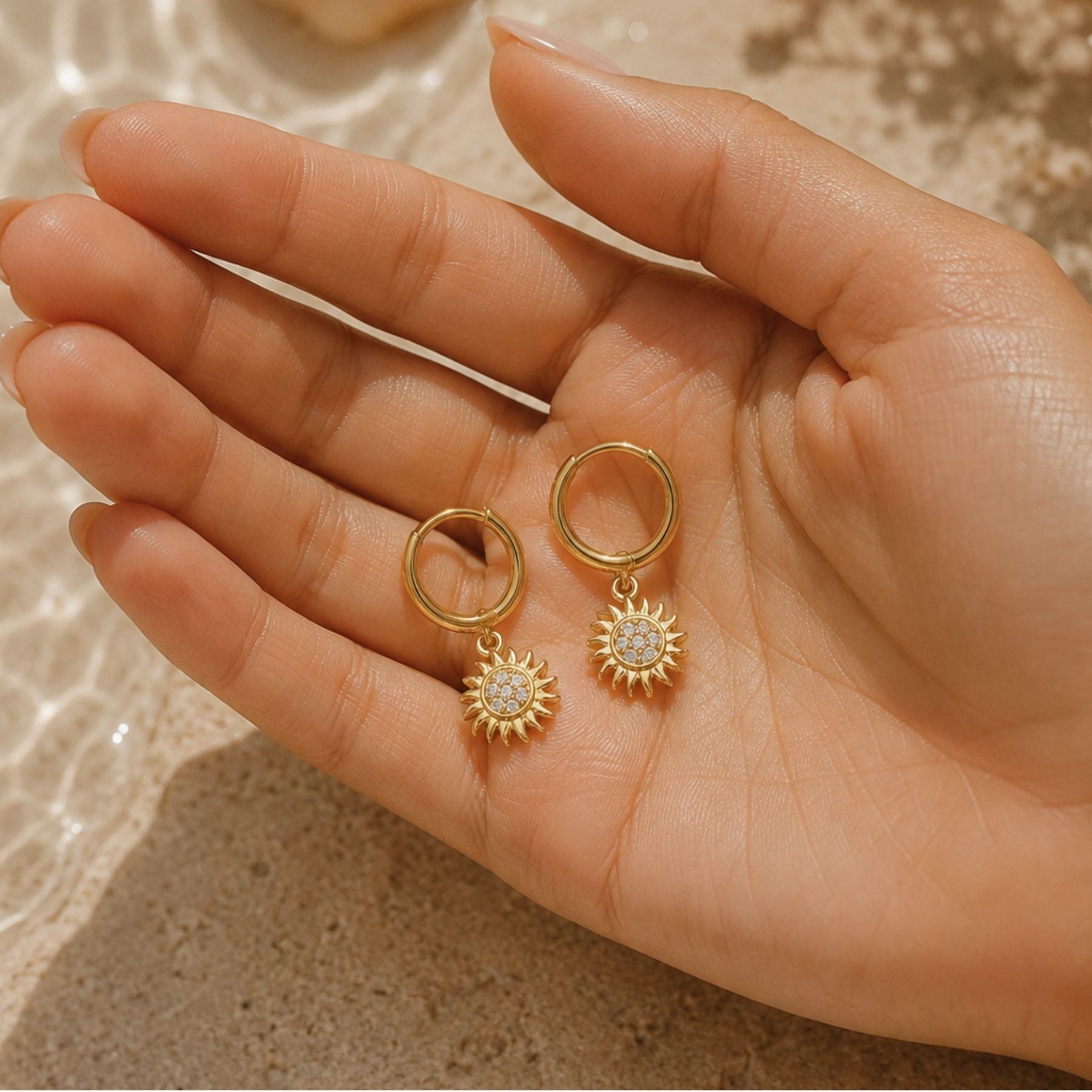 Pair of Helio gold sun hoop earrings with zirconia charms held in hand