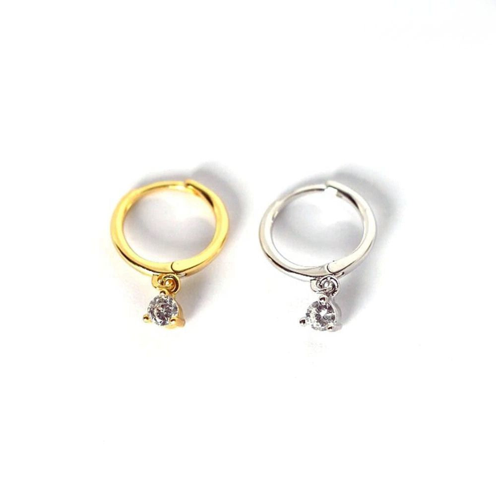 Minimalist huggie hoop earrings in gold and silver with a small dangling cubic zirconia stone.