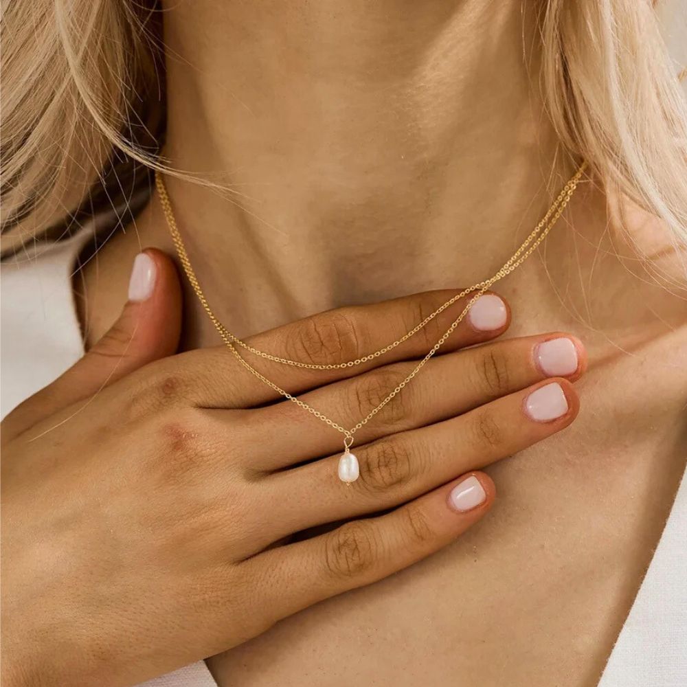 Minimalist layered gold necklace with a small freshwater pearl pendant on model.